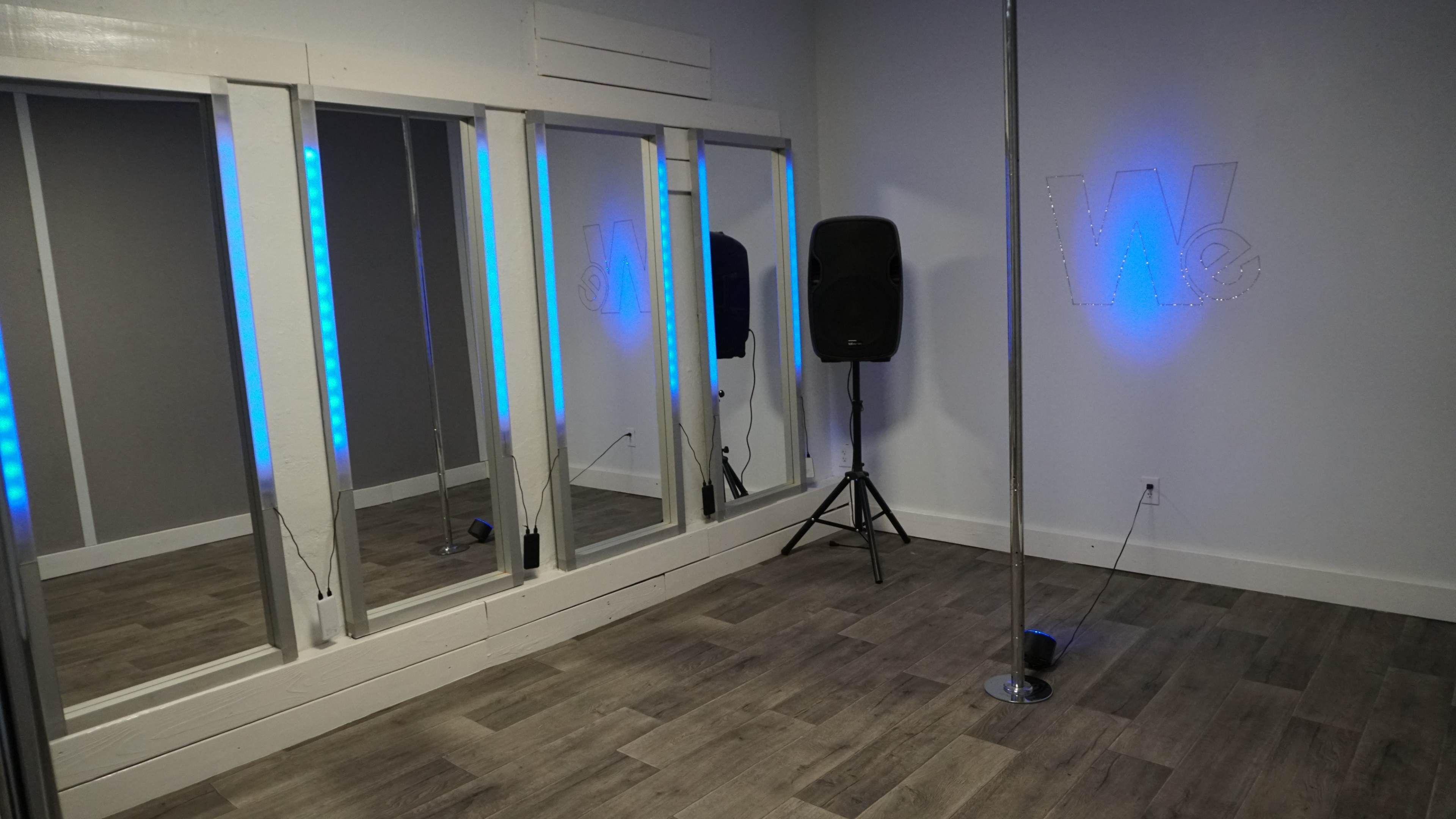 A room with mirrored walls, a speaker, and a dance pole, illuminated by blue LED lights.