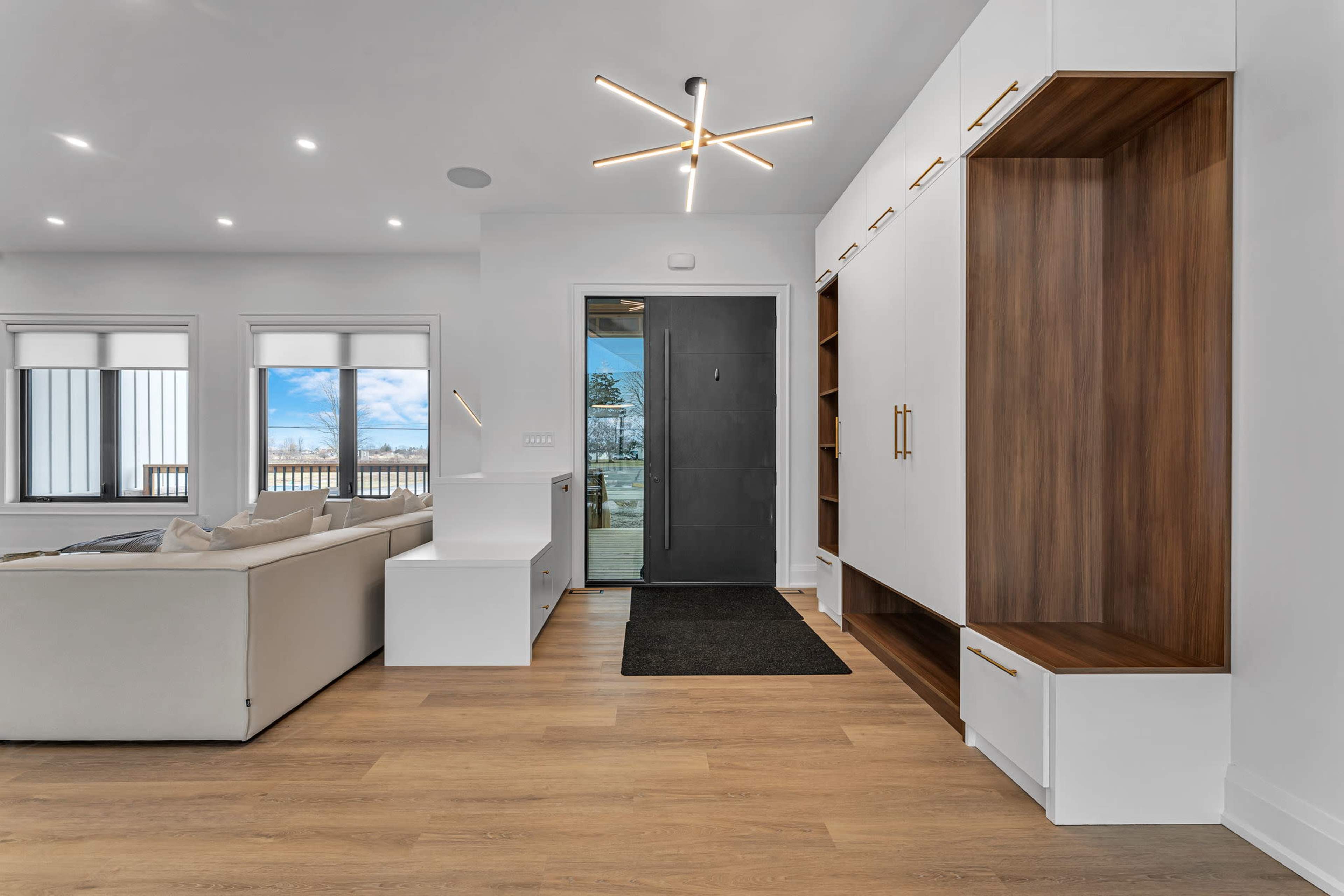 A modern living space with a white sofa, minimalistic furniture, and a dark front door leading outside.