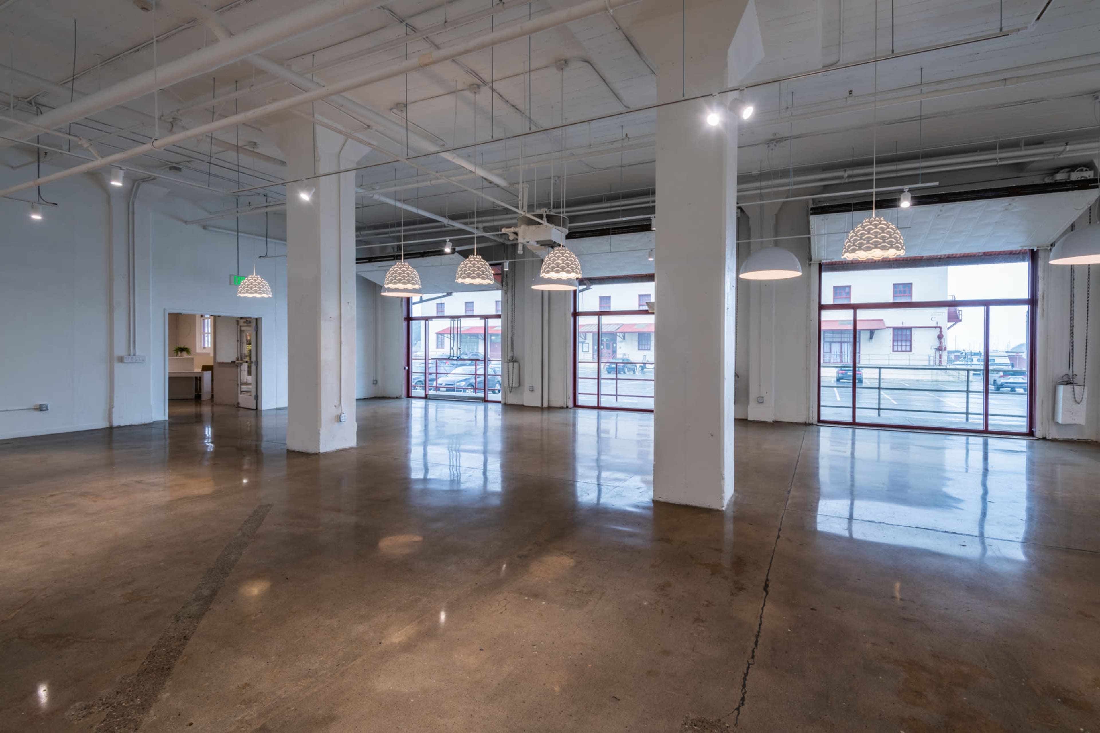 A spacious, empty room with polished concrete floors, white walls, and several pendant lights hanging from the ceiling.