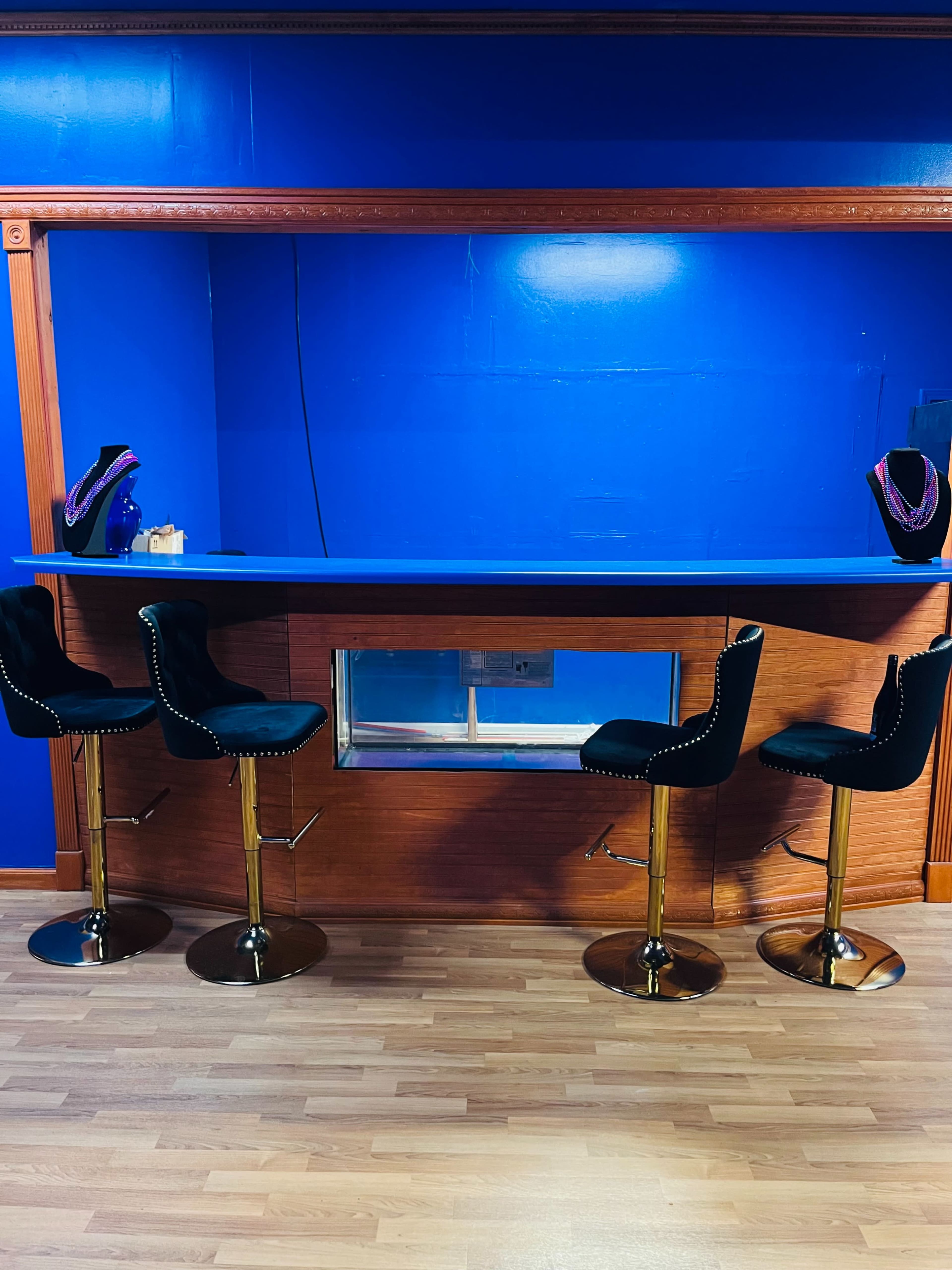 The image shows a bar area with four black leather stools in front of a blue wall and a wooden counter.
