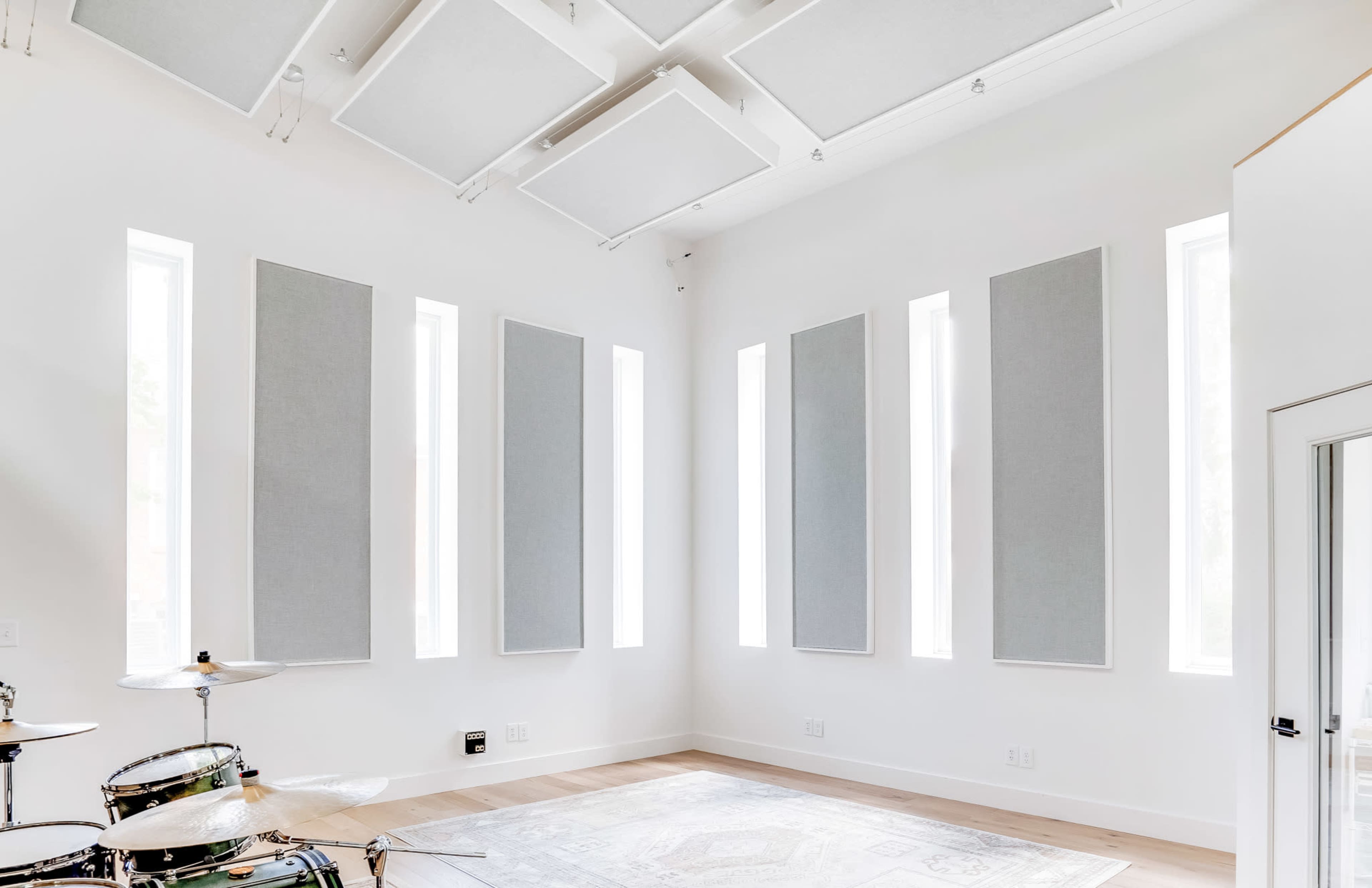 A spacious music studio featuring a drum set and tall, rectangular soundproof panels on white walls.