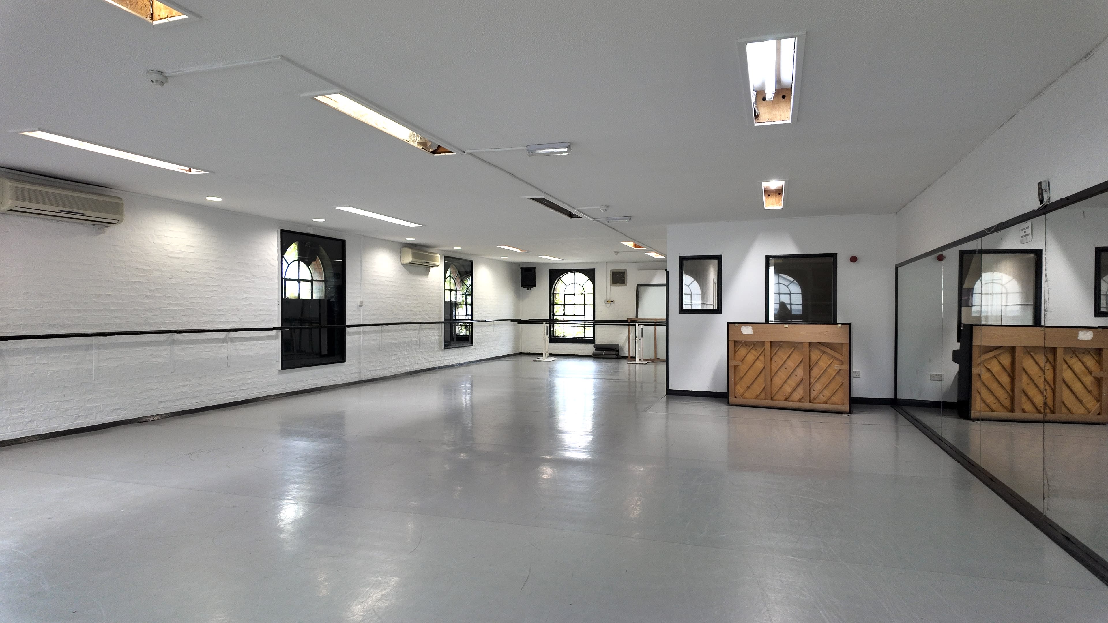 The image shows a spacious, well-lit dance studio with a polished floor, mirrors on one wall, and a reception area featuring a wooden counter.
