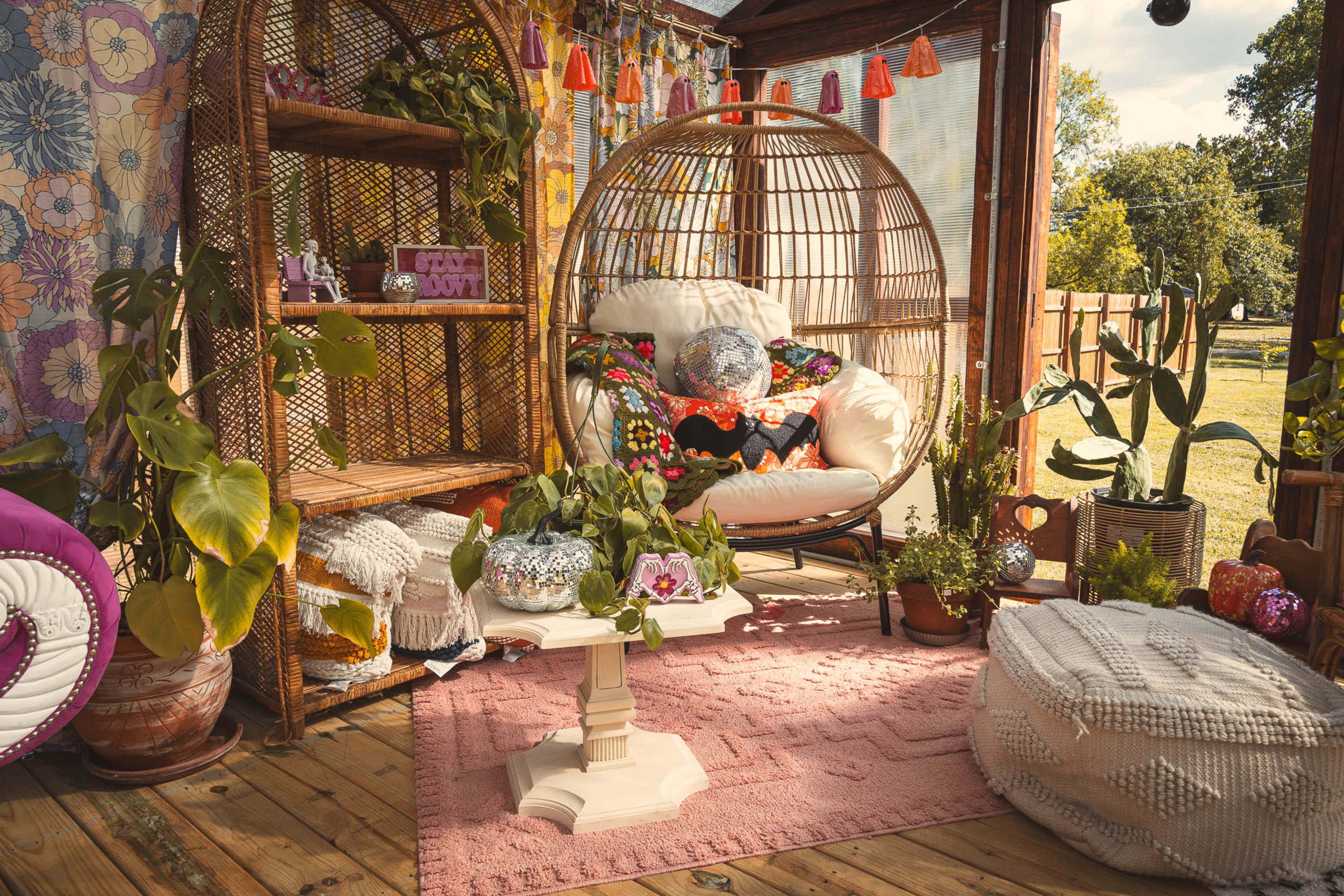 The scene features a cozy indoor space with a hanging chair surrounded by vibrant plants, decorative shelves, and a small table on a textured rug.