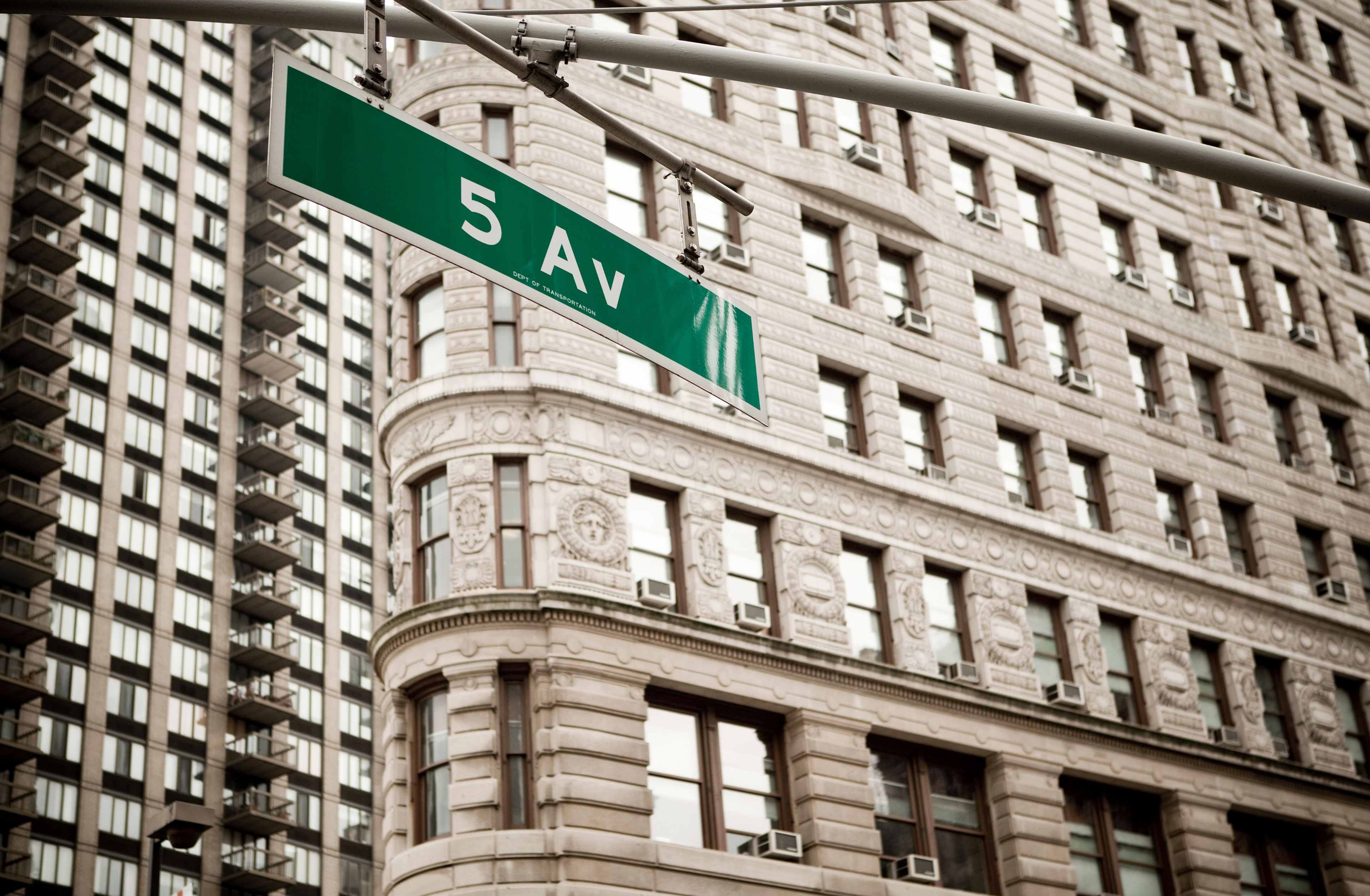 A green street sign labeled "5 Av" hangs above a brick building with decorative architectural details.