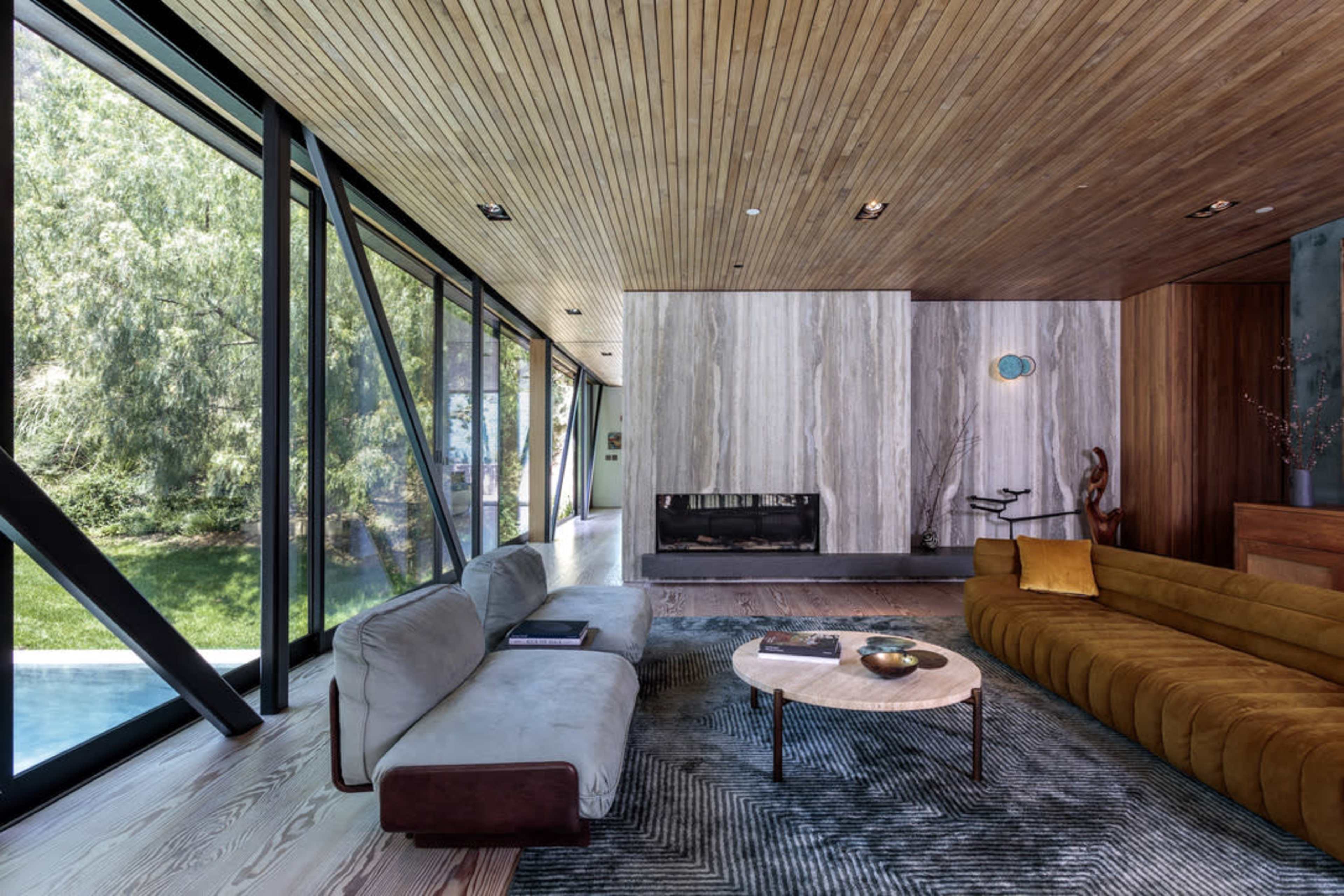 The scene features a modern living room with large windows, a wooden ceiling, a mix of seating options, and a central coffee table.