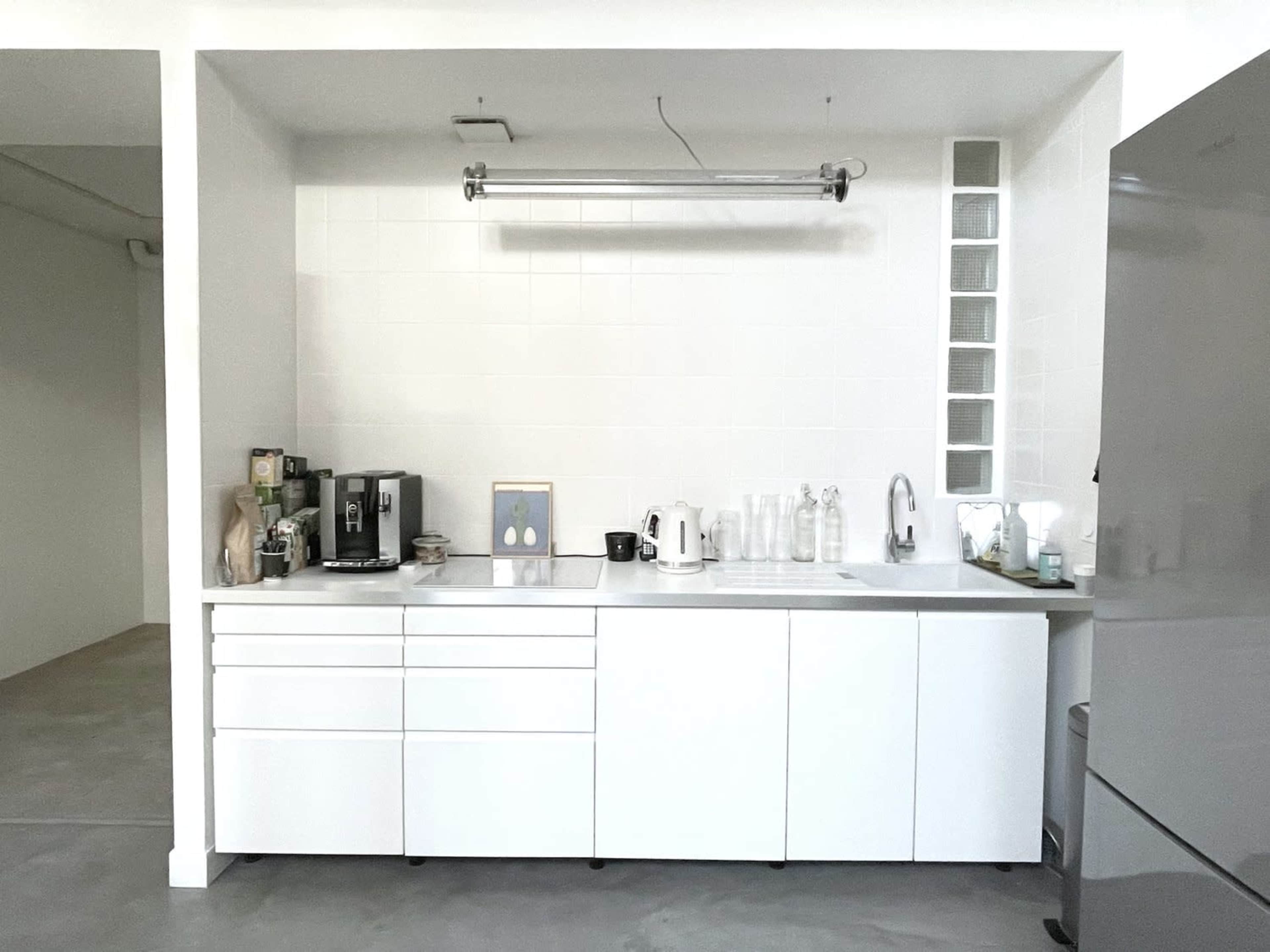 A minimalist kitchen with a white cabinetry, a coffee maker, a kettle, and several bottles on the countertop.