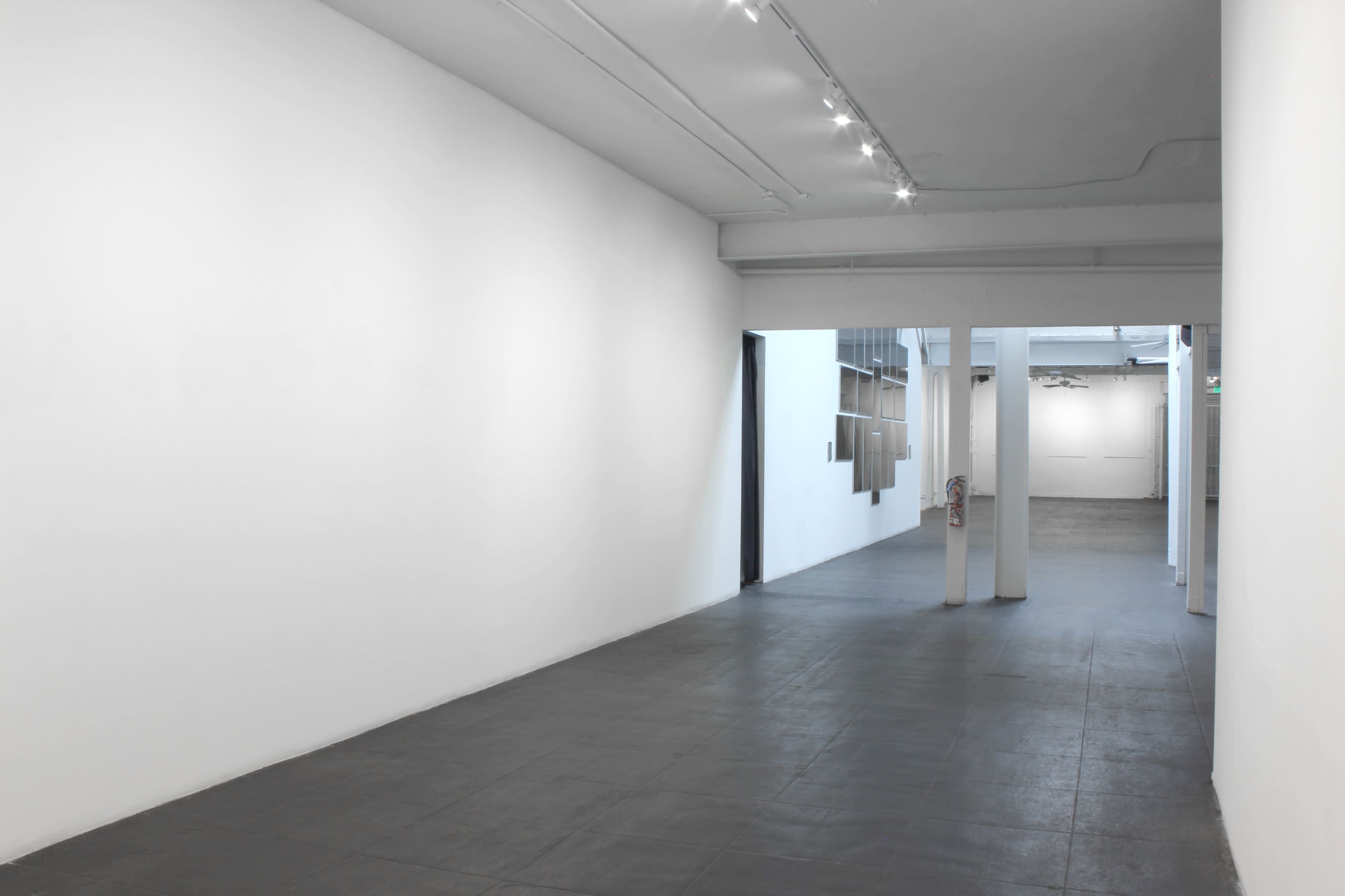 A spacious gallery interior with white walls, a dark tiled floor, and track lighting.