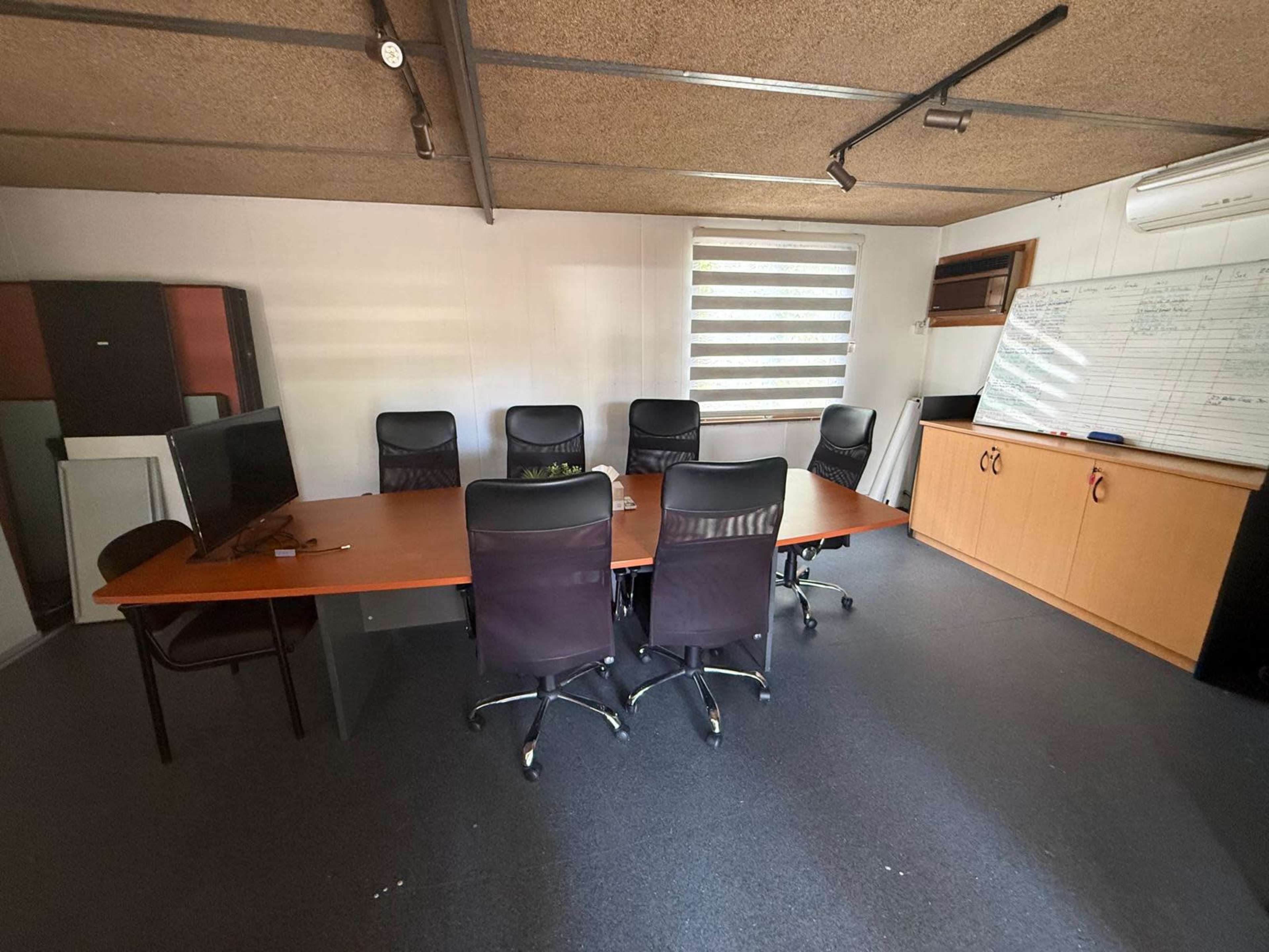 The image shows a meeting room with a large wooden table surrounded by black office chairs and a wall-mounted whiteboard.