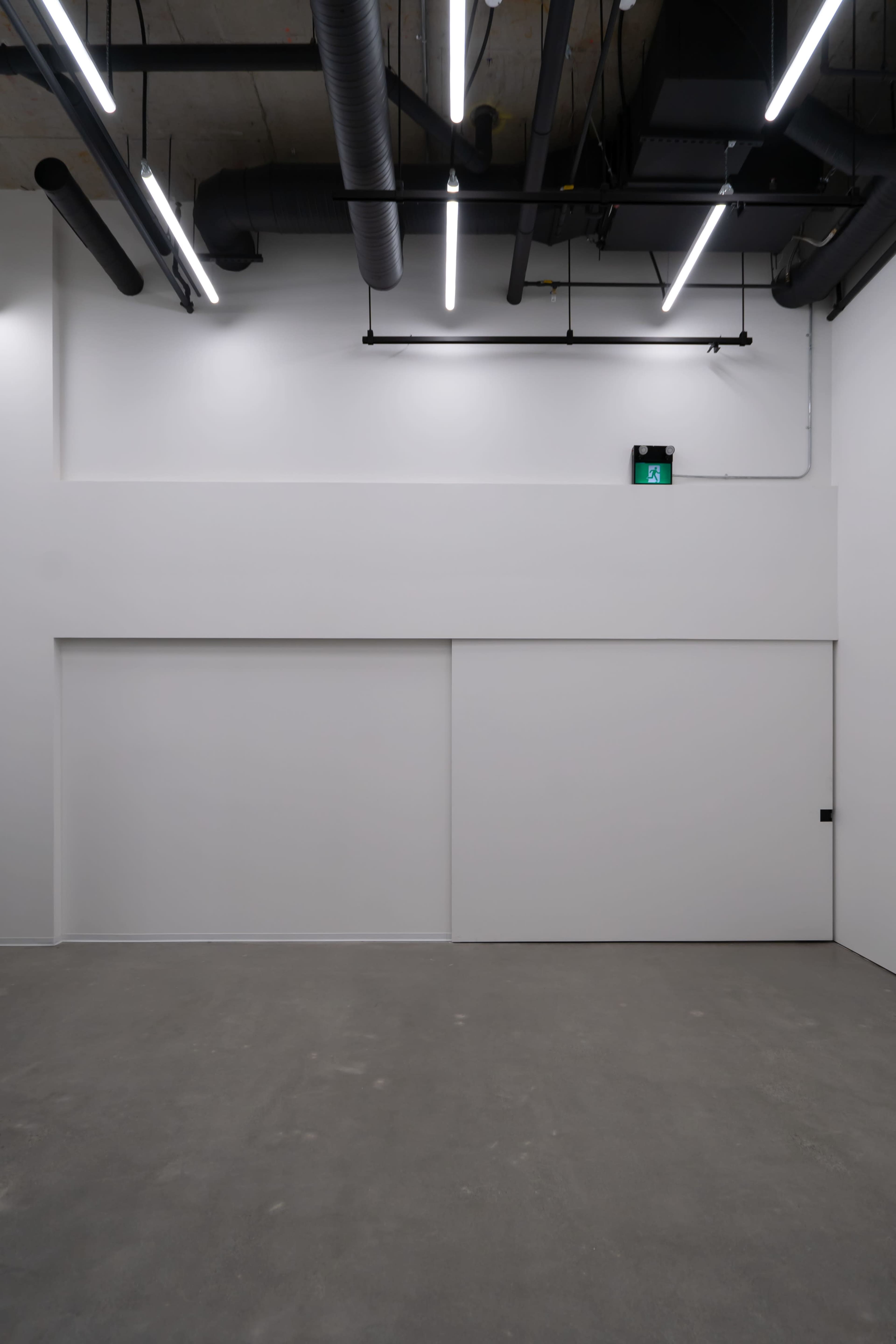 An empty, minimalist interior space with white walls, concrete flooring, and overhead lighting fixtures.