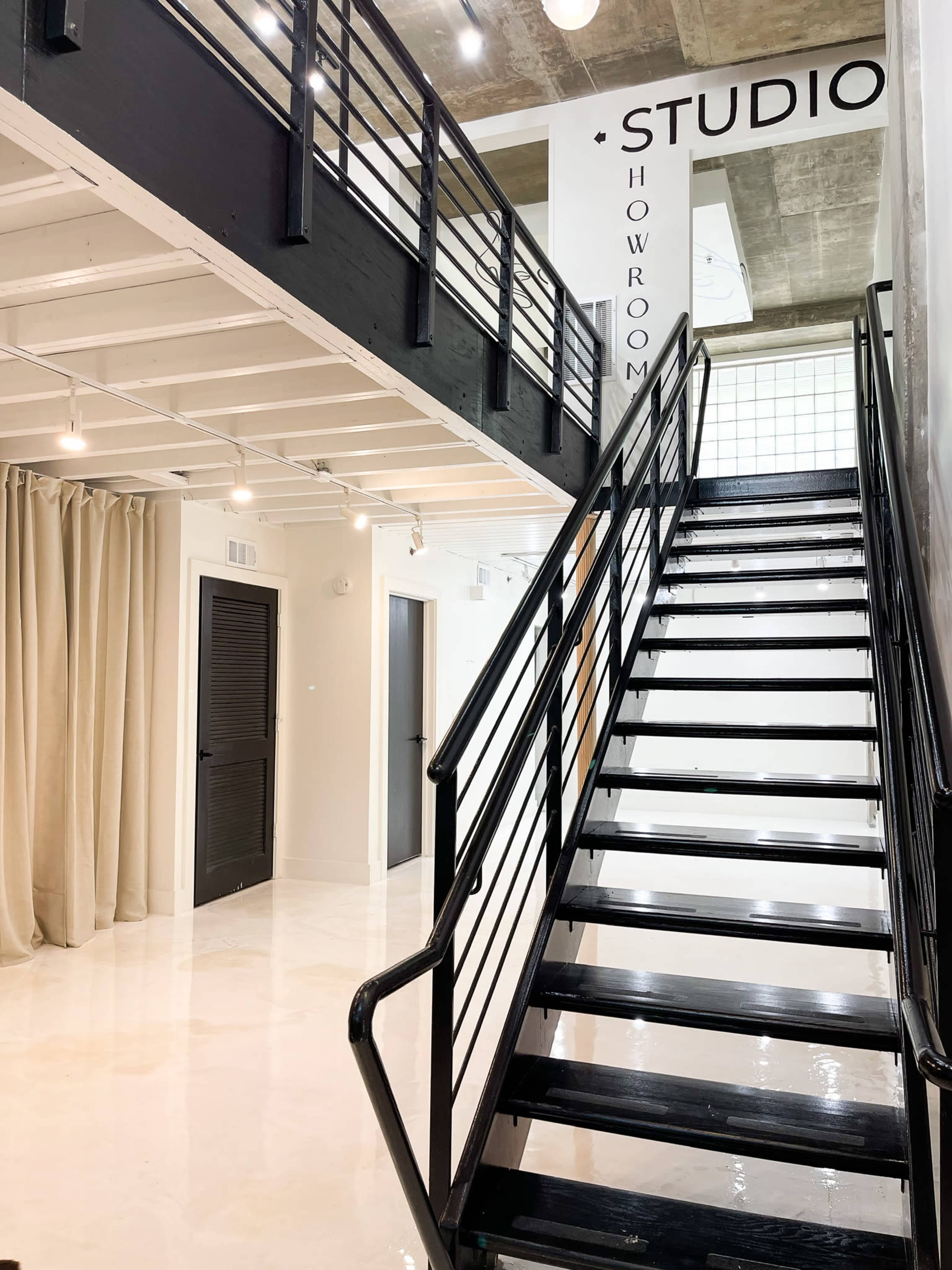 A modern interior with a black staircase leading to an upper level, featuring white walls and sheer curtains.