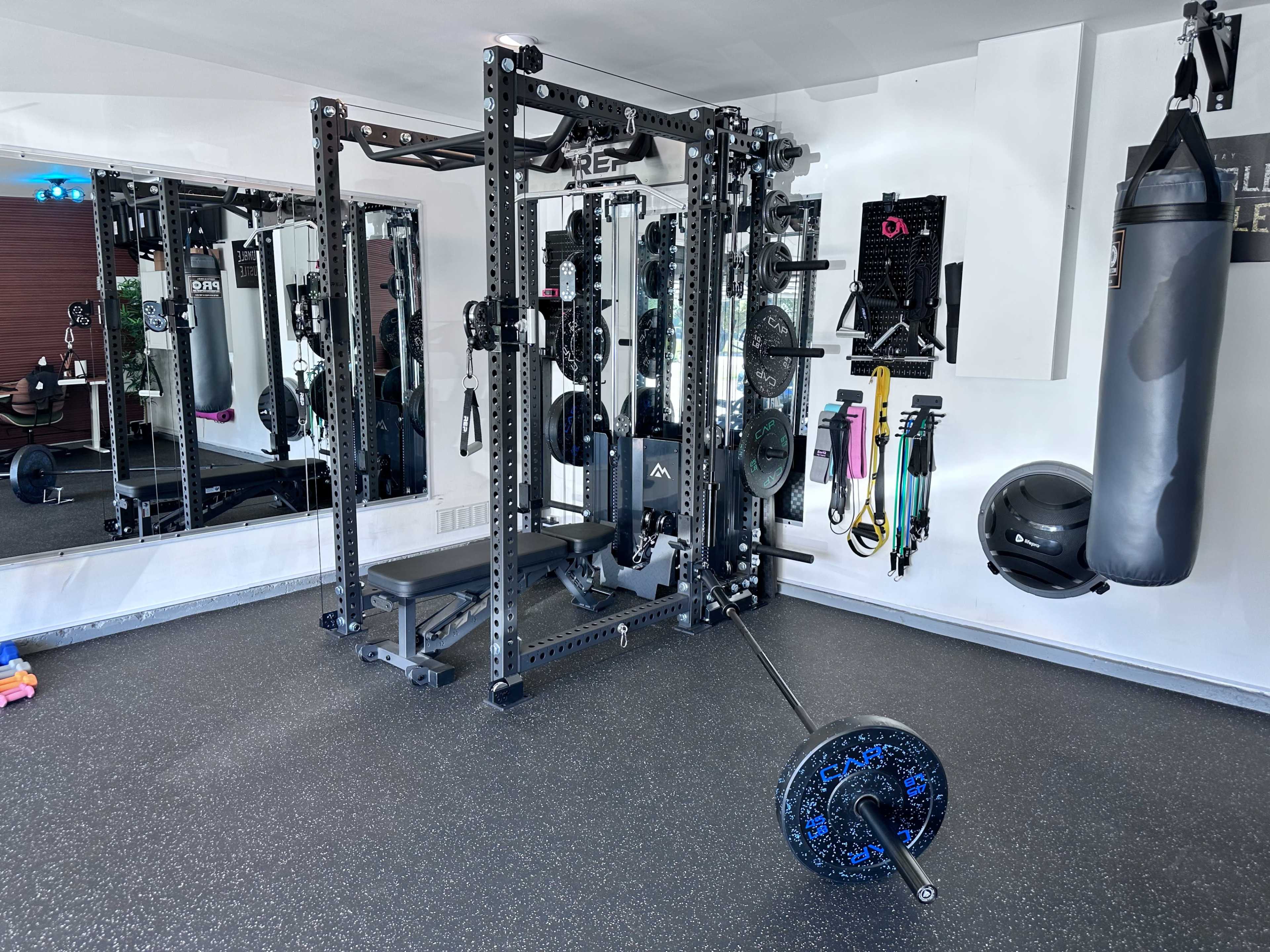 The image shows a well-equipped home gym featuring a power rack, weightlifting barbell, and various exercise equipment mounted on the walls.