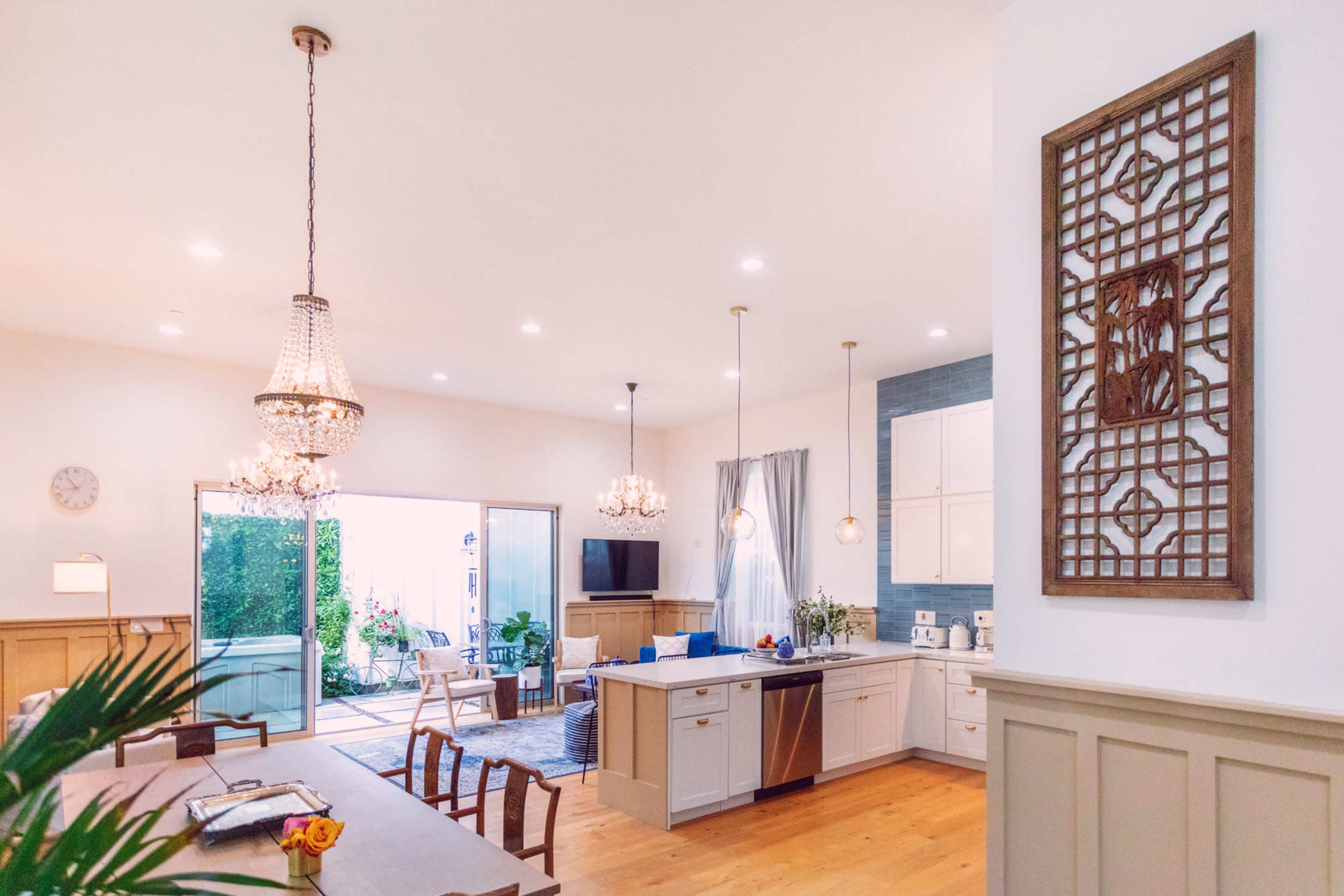 A modern open-concept kitchen and dining area features a large table, elegant chandeliers, and a sliding glass door leading to an outdoor space.