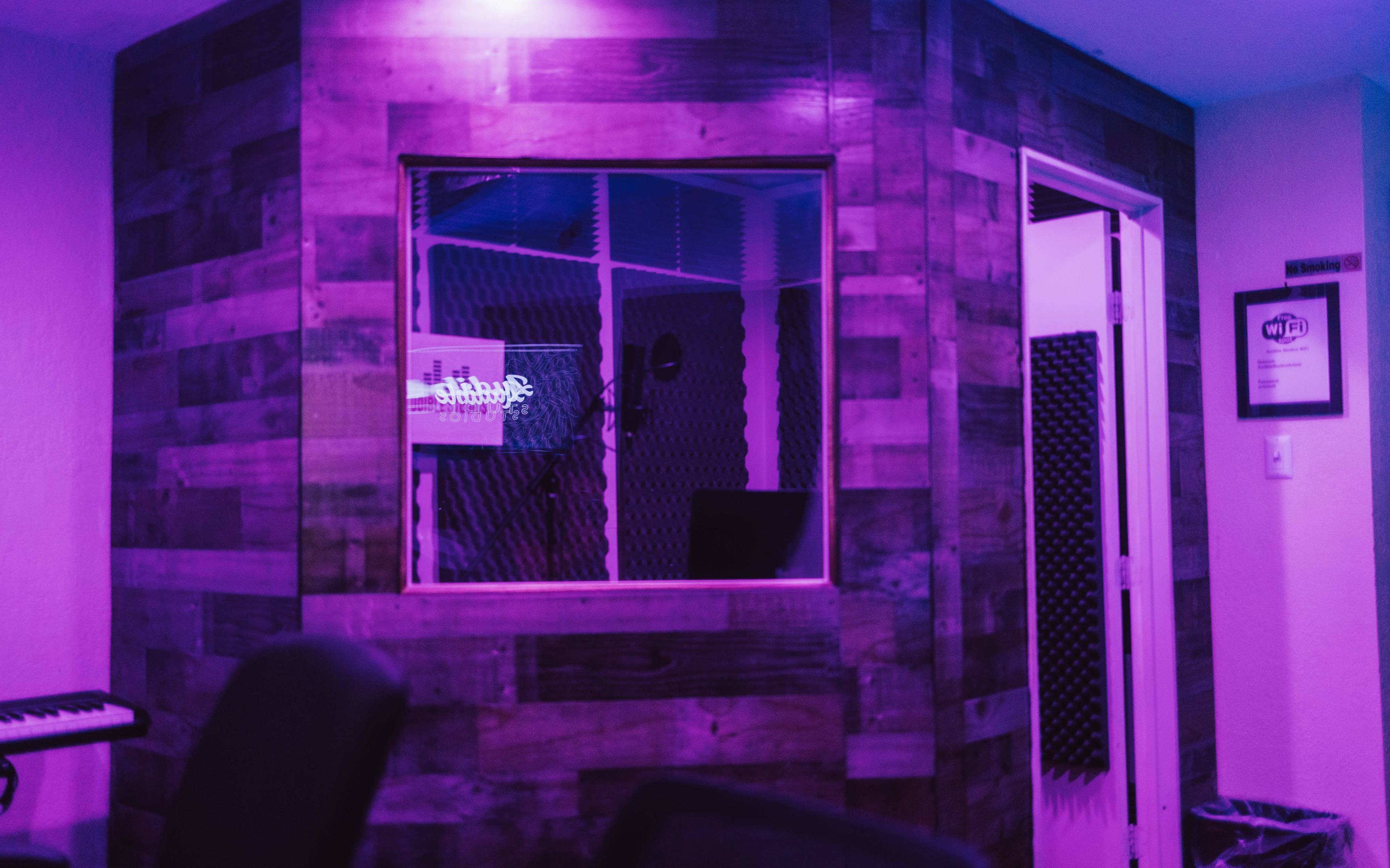 A music studio with wooden walls, a soundproof recording booth, and purple lighting.