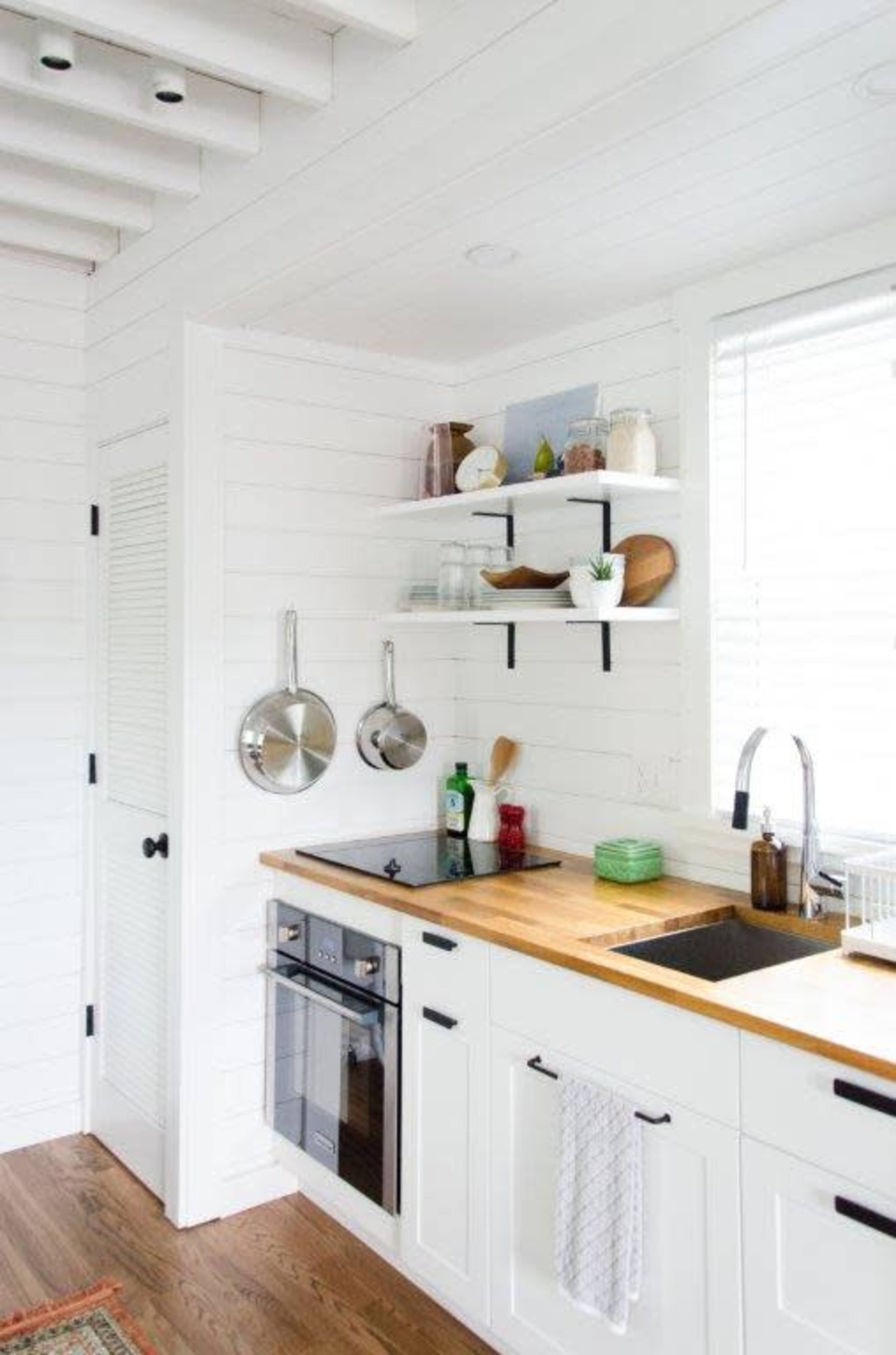 The image shows a modern kitchen with white shiplap walls, wooden countertops, and open shelving displaying kitchenware.