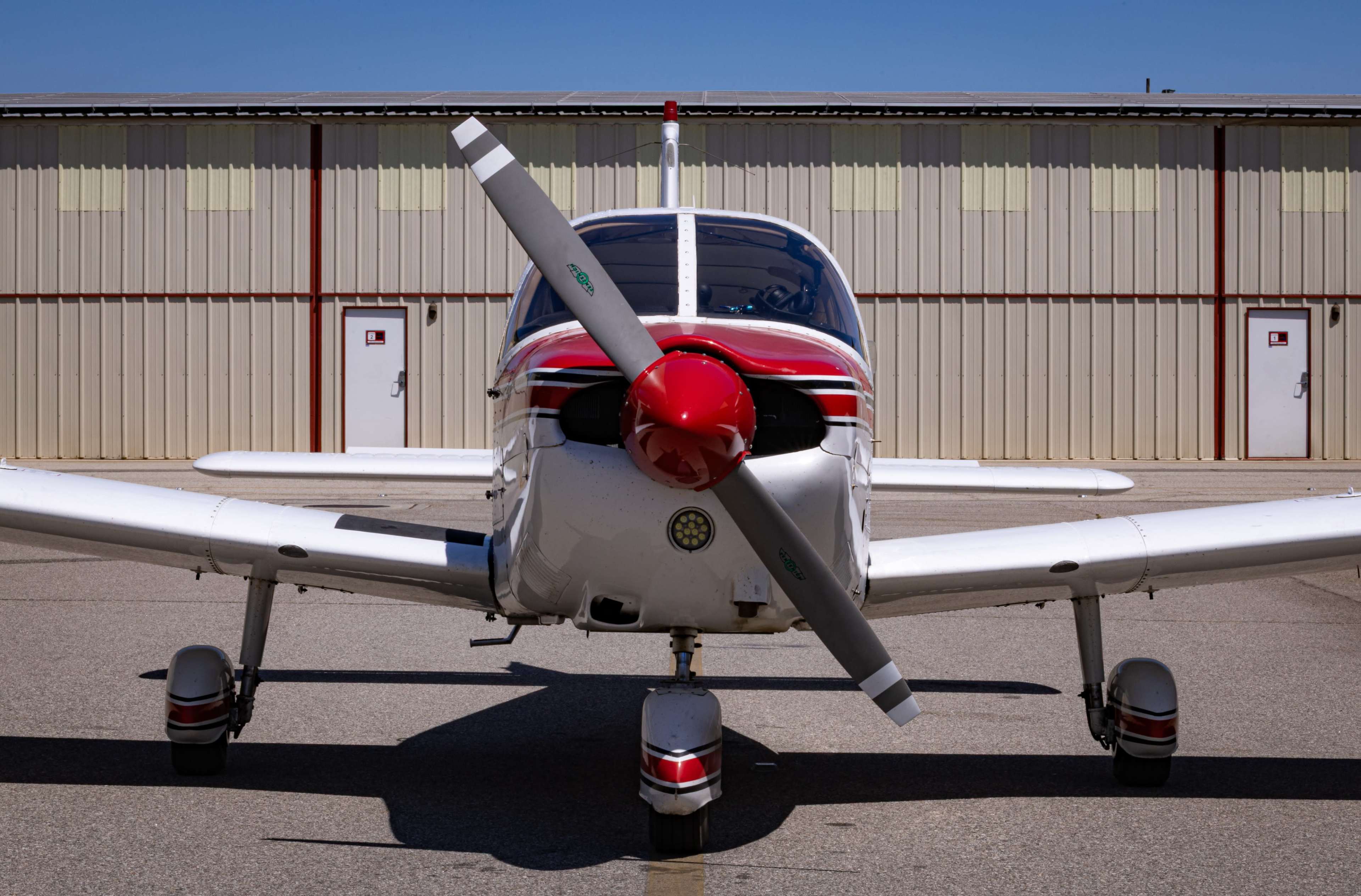 A small white and red aircraft with a propeller is parked in front of a hangar.