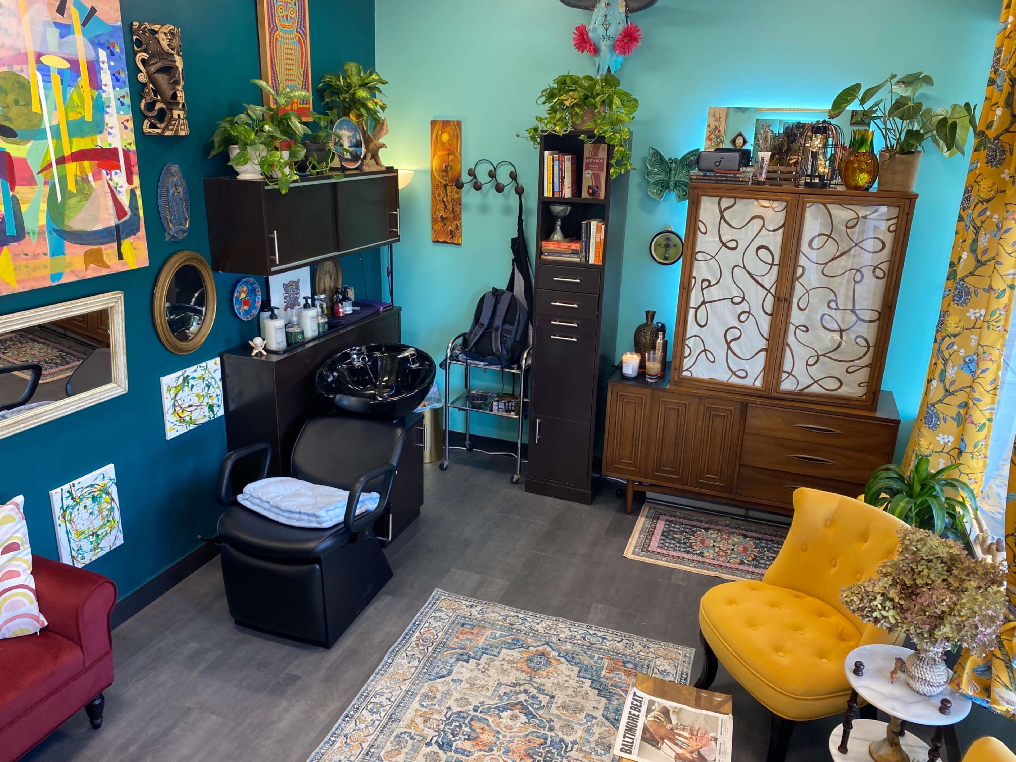 The image depicts a colorful salon interior featuring a stylist chair, a shampoo basin, and various plants along with decorative furniture and artwork on the walls.