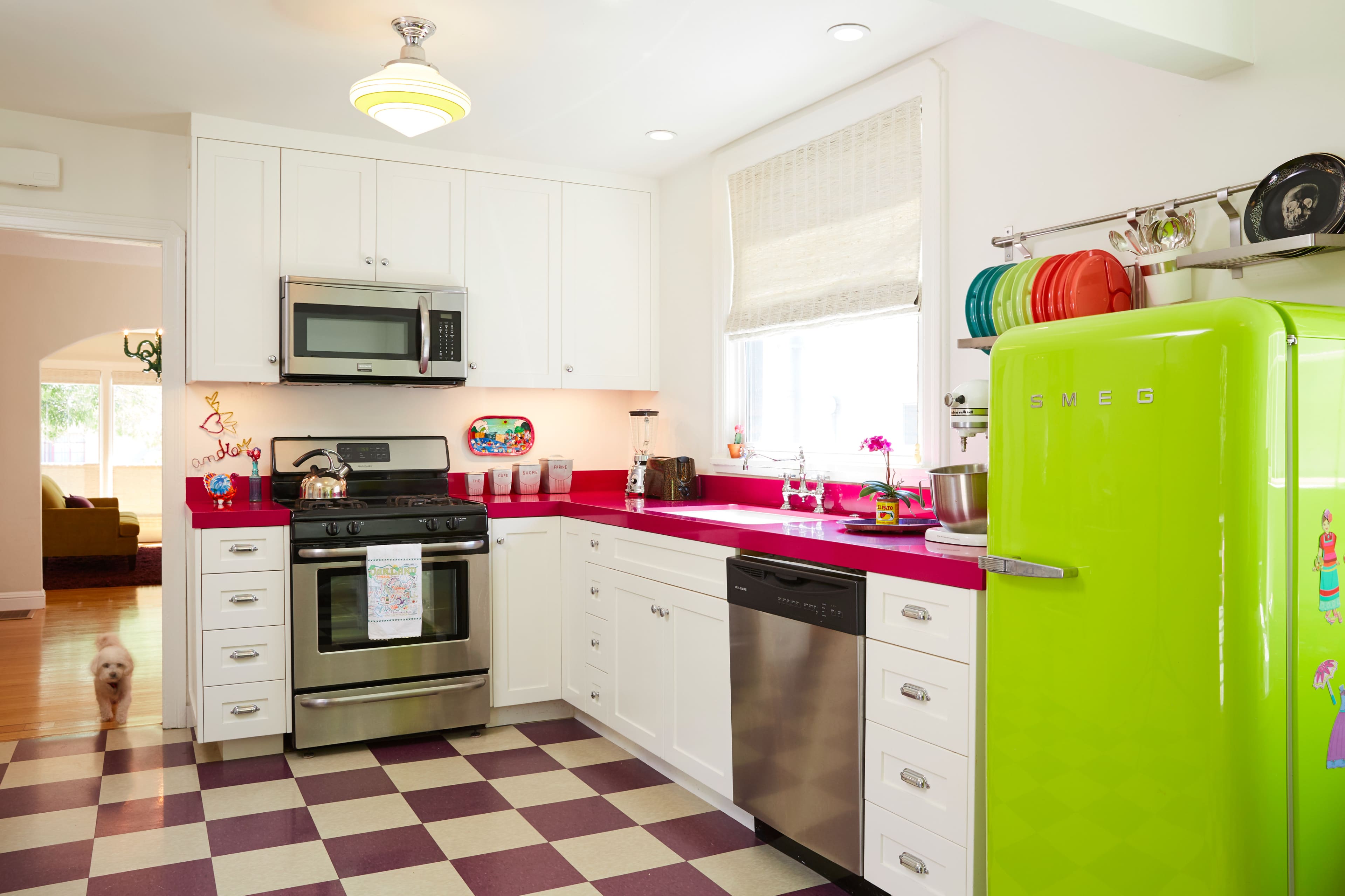 A brightly colored kitchen features white cabinets, stainless steel appliances, and a retro green refrigerator on a checkered floor.
