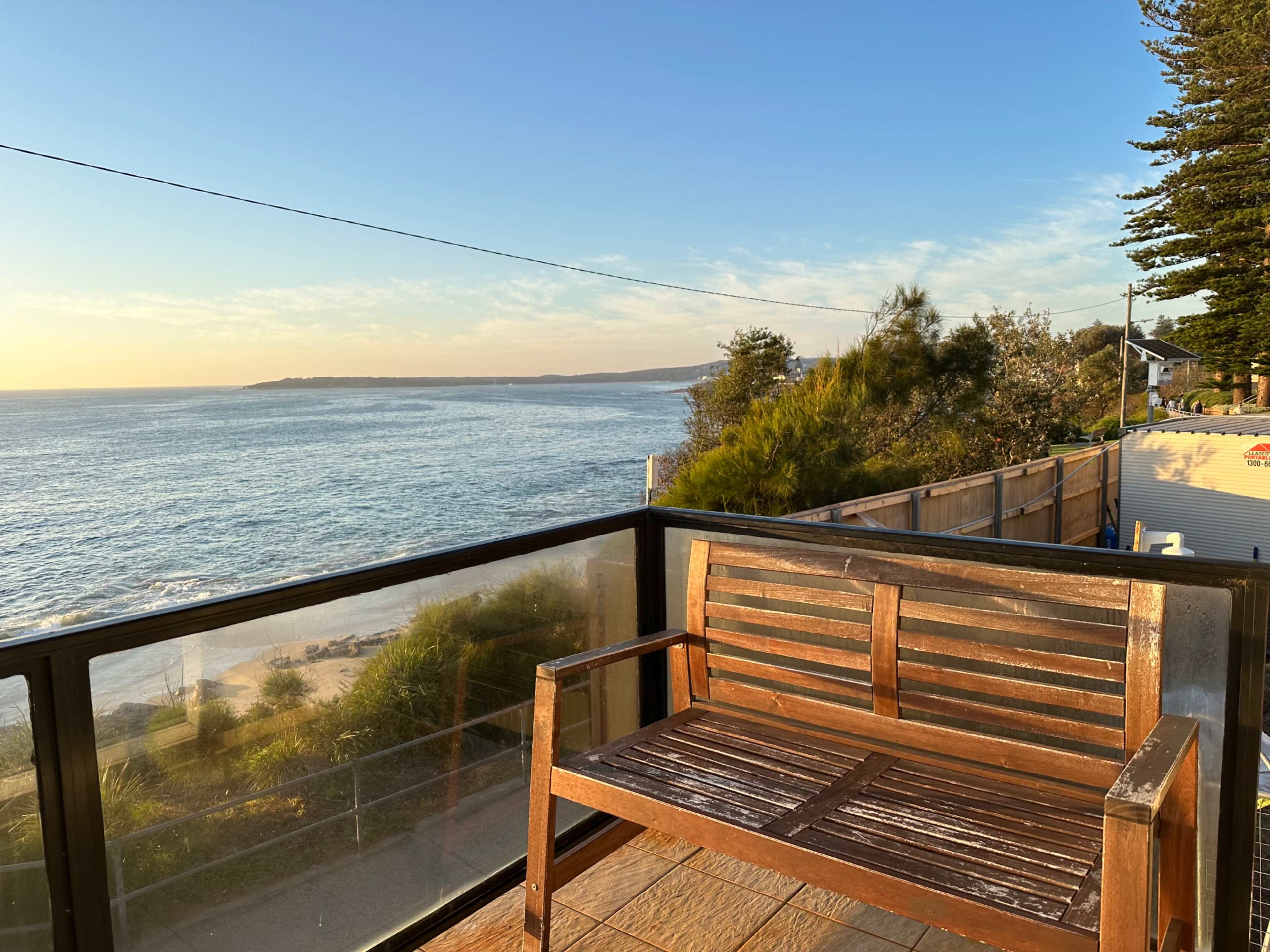 A wooden bench is positioned on a balcony overlooking the ocean at sunset.