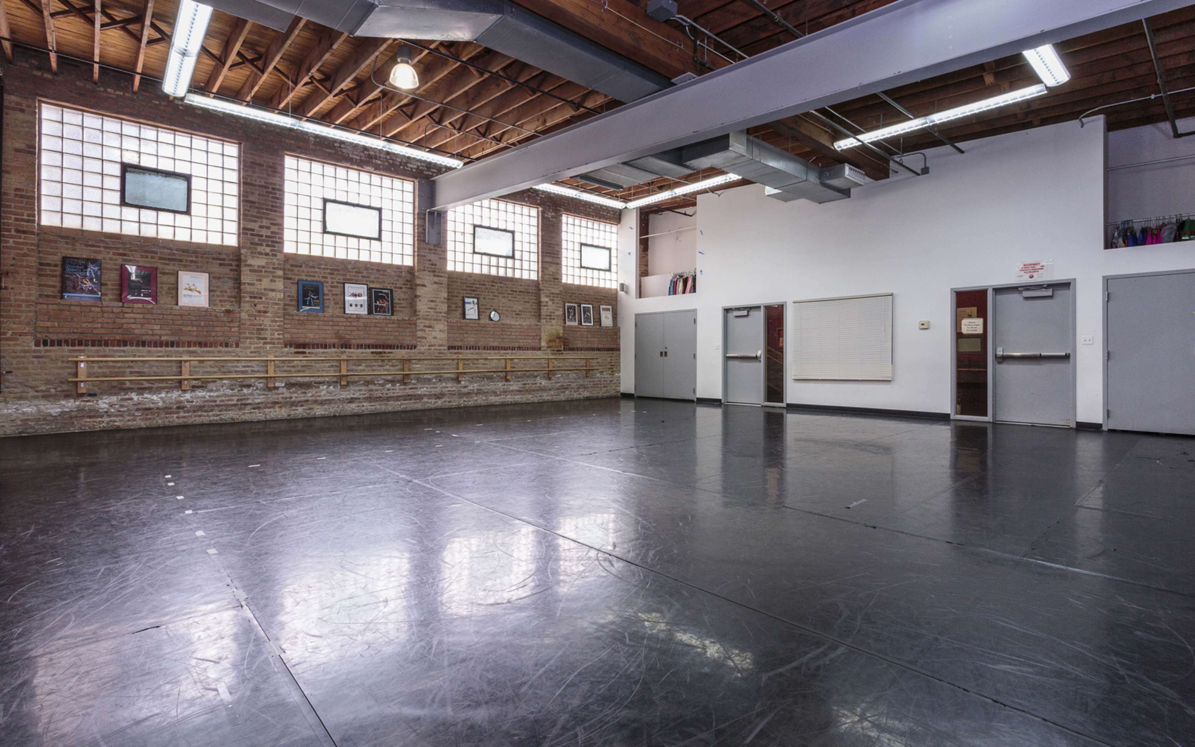 A spacious dance studio with a polished black floor, large windows, and a mirrored wall.