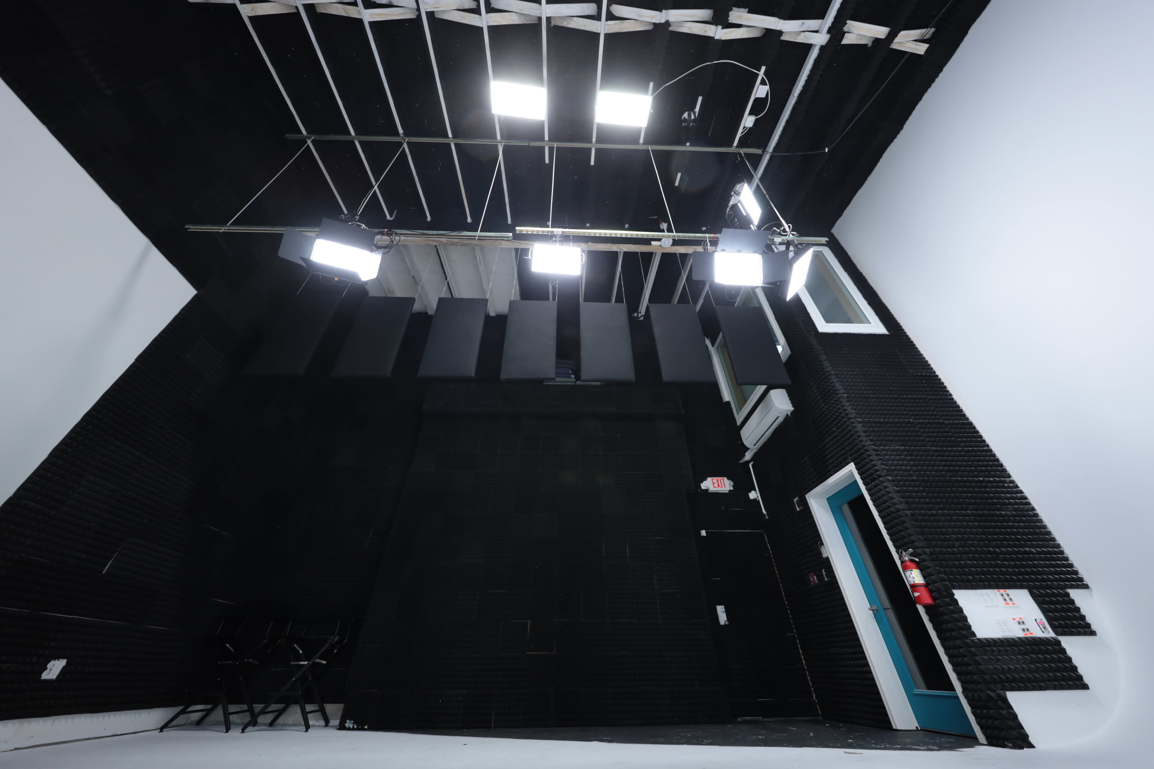 A dimly lit recording studio with black sound-absorbent panels on the walls and bright lights mounted on the ceiling.