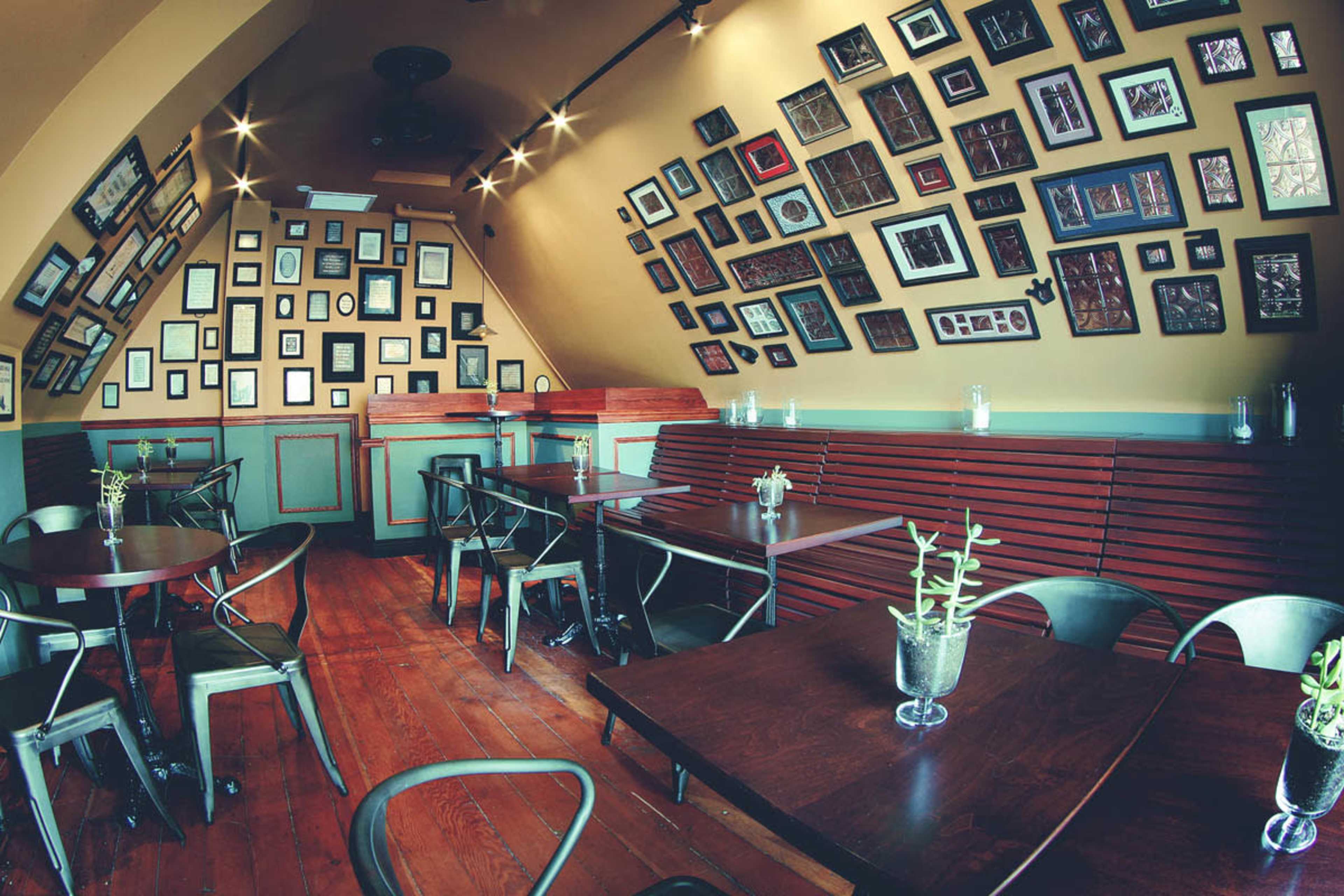 The image shows a cozy restaurant interior featuring wooden floors, green walls, and a wall adorned with various framed pictures.