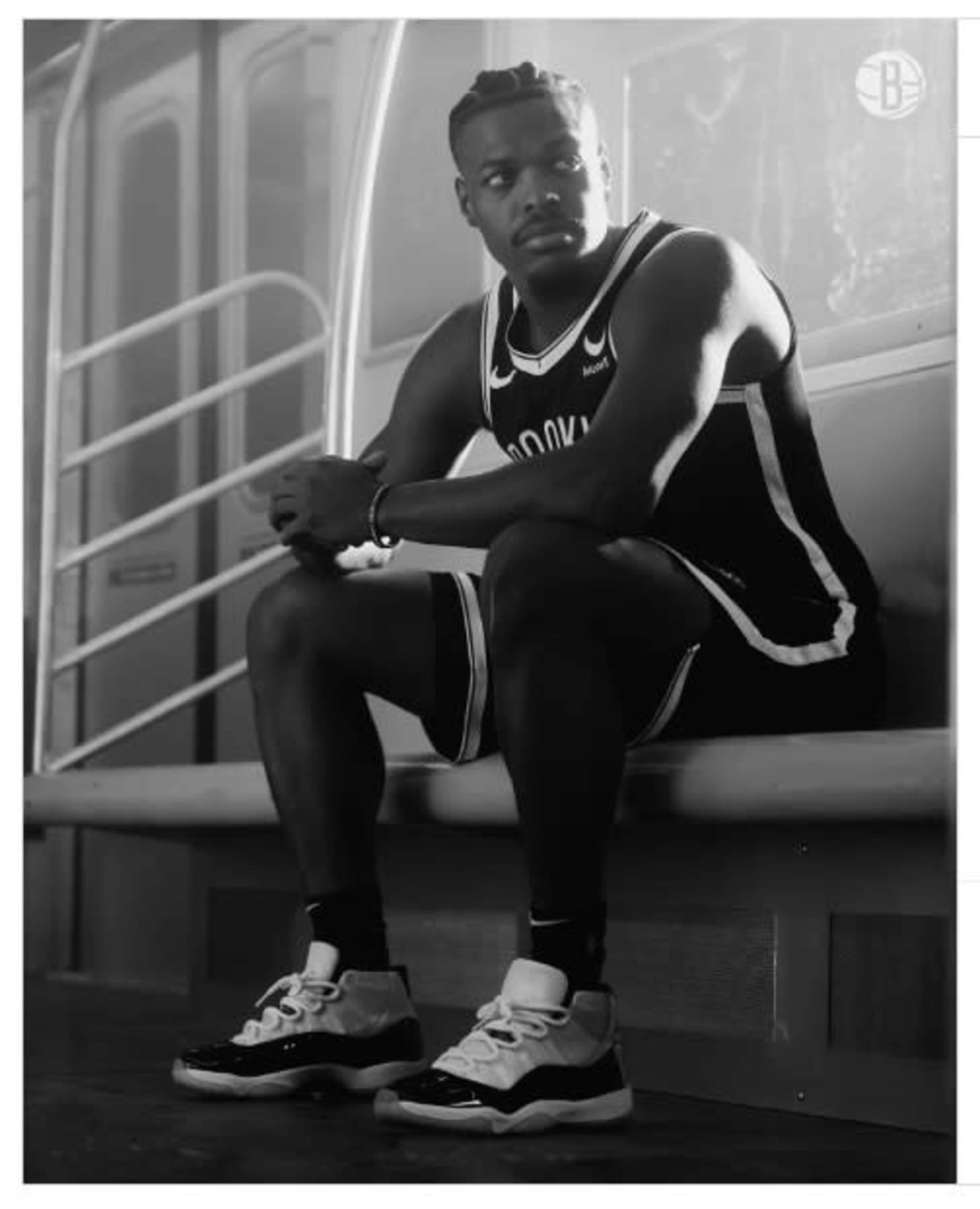 A man in a black and white basketball uniform sits on a subway bench, looking contemplatively ahead.