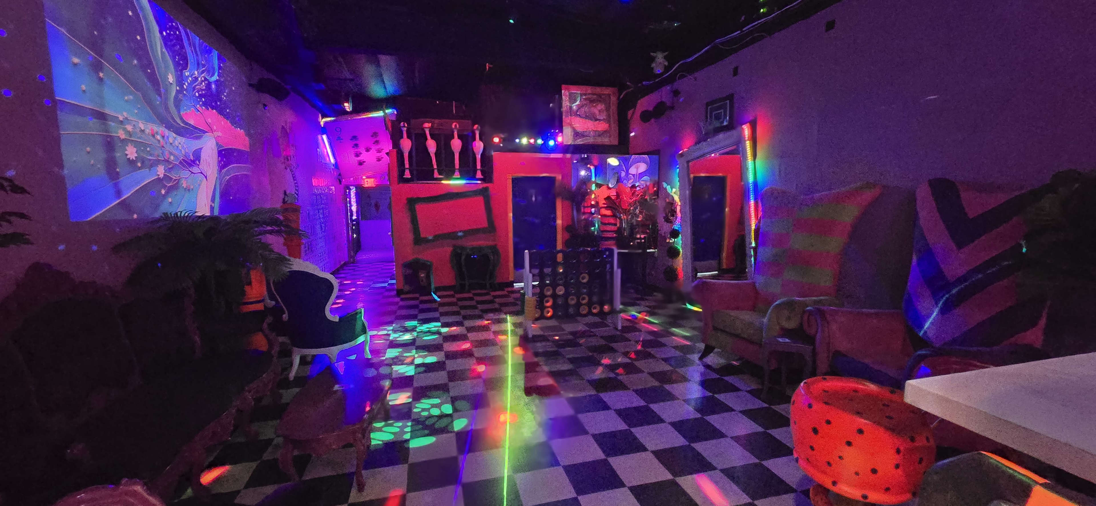 A colorful, vibrant interior of a venue with checkered flooring, eclectic seating, and projection lights creating patterns on the walls and floor.