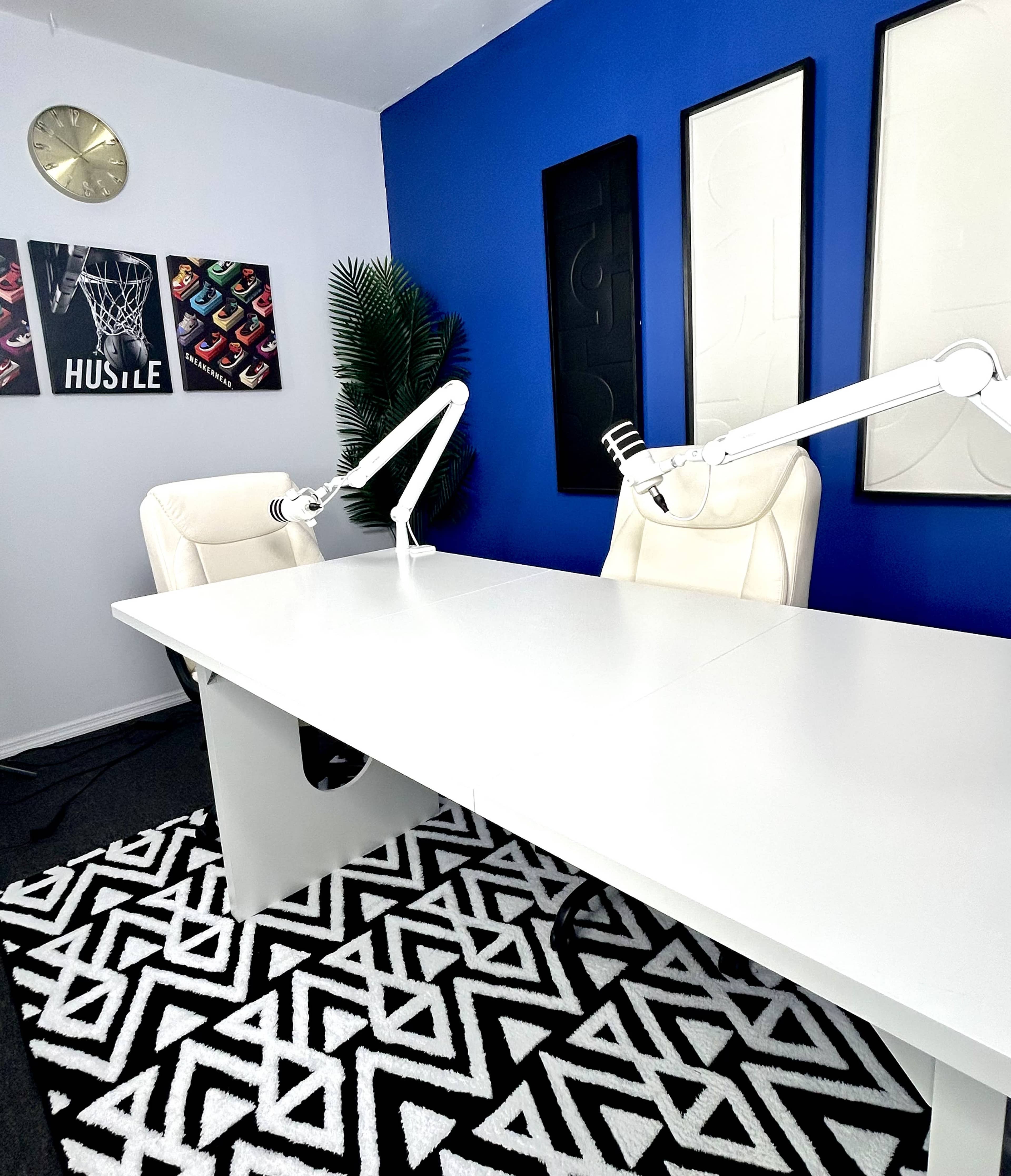 The image shows a modern office space with a large white table, two ergonomic chairs, and a blue accent wall featuring framed artwork.