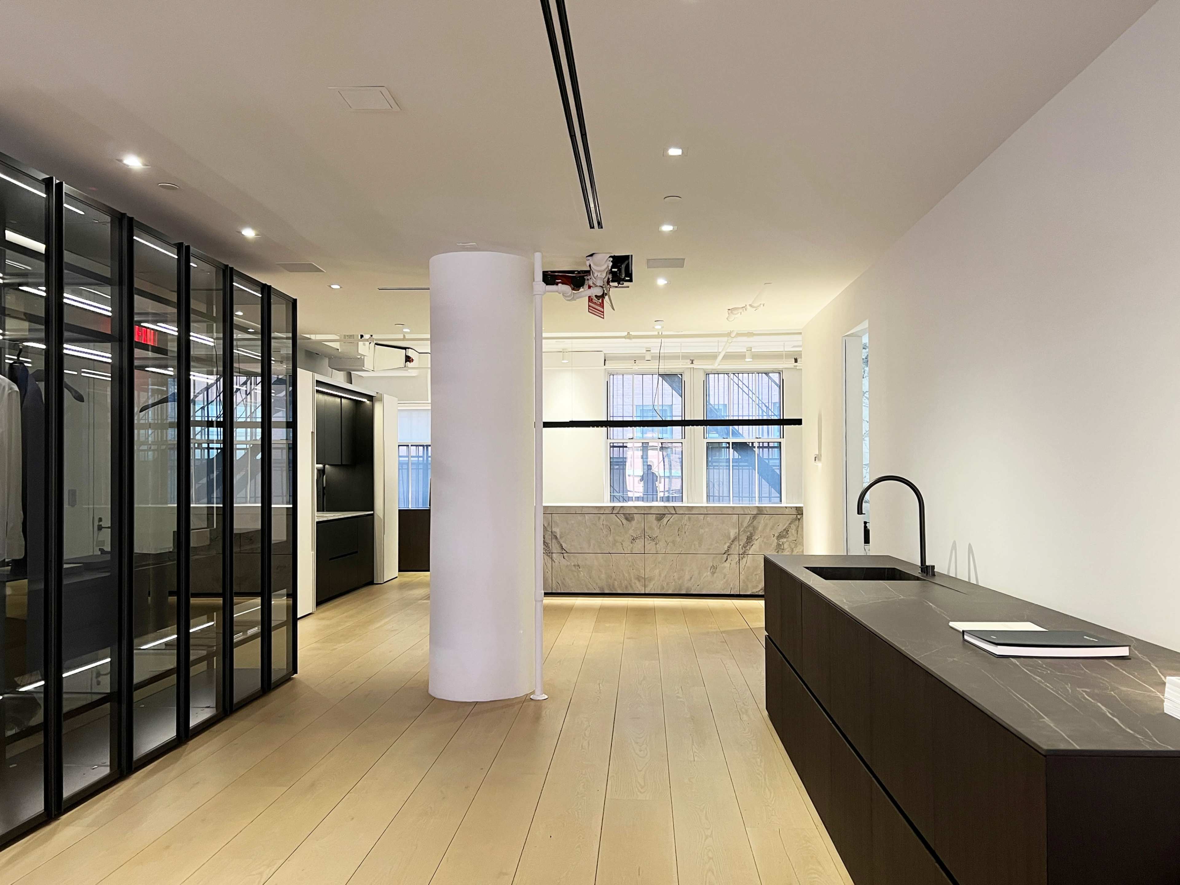 A modern office space featuring wooden flooring, a large marble counter, and glass walls enclosing a clothing display area.