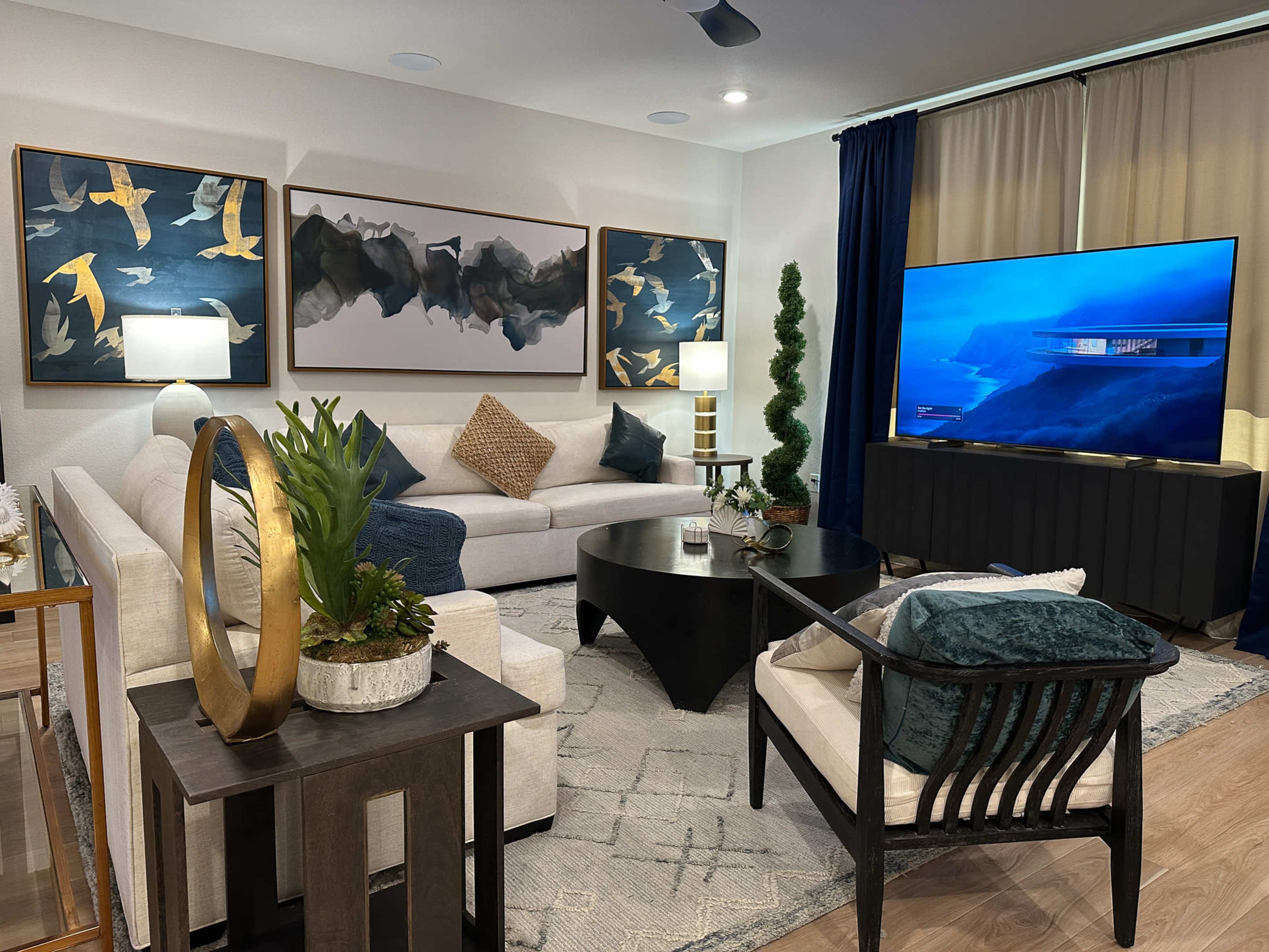 The living room features a modern seating arrangement with a large sectional sofa, a circular coffee table, and an entertainment unit displaying a television, complemented by decorative artwork and potted plants.