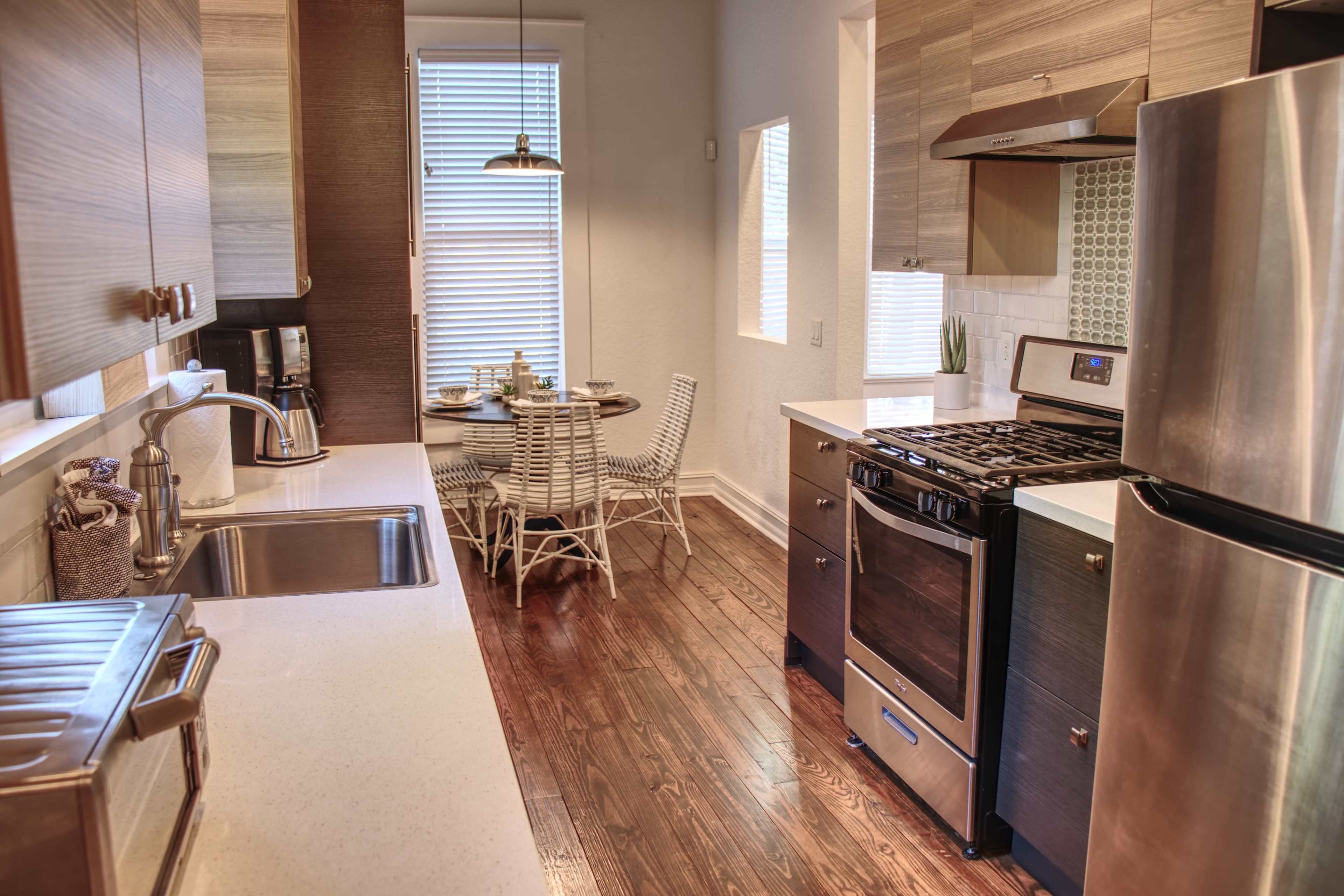 A modern kitchen with stainless steel appliances, wooden cabinetry, and a small dining area featuring a round table and chairs.
