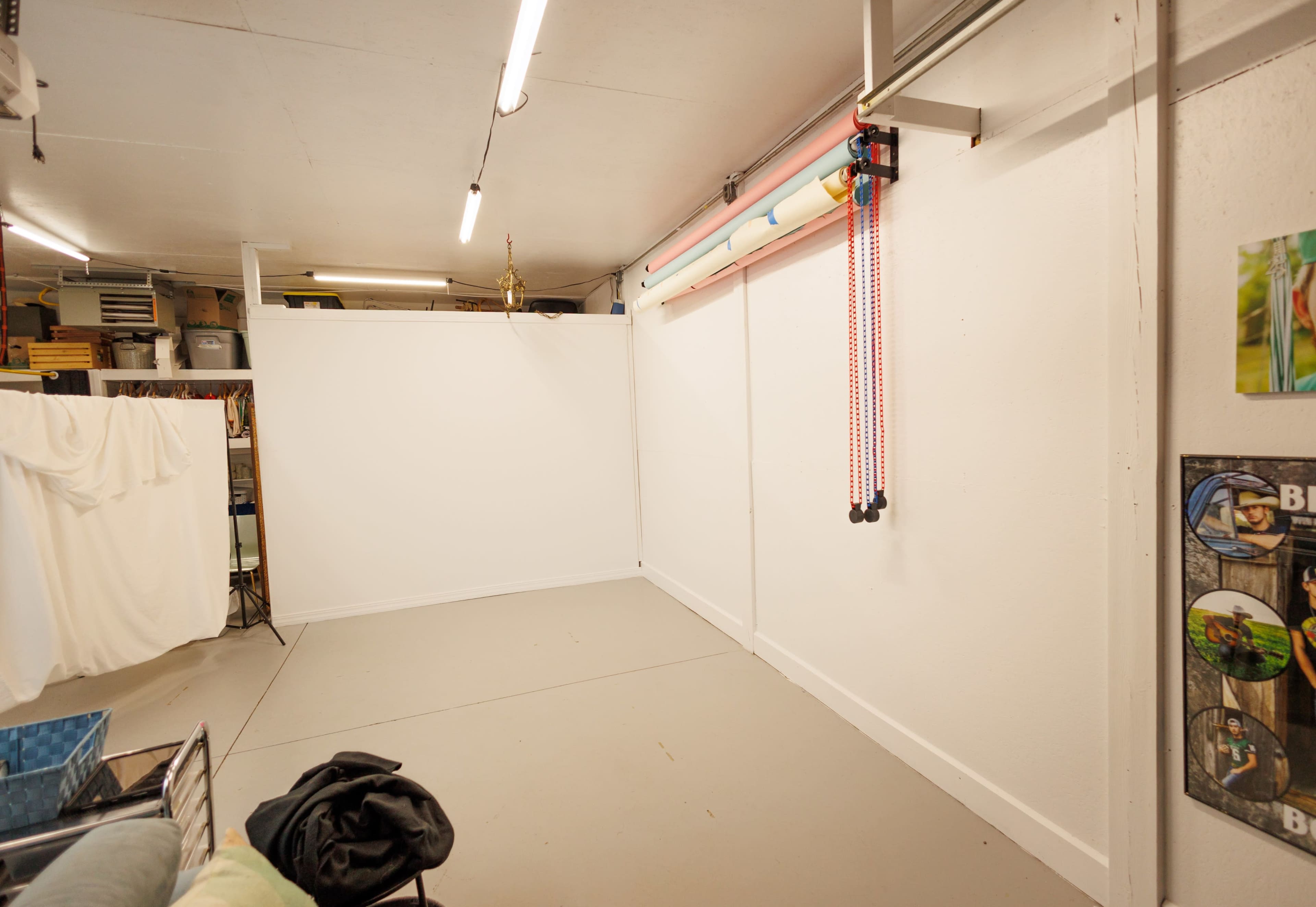 The image shows a clean, empty room with white walls, a concrete floor, and colorful tubes attached to the ceiling.
