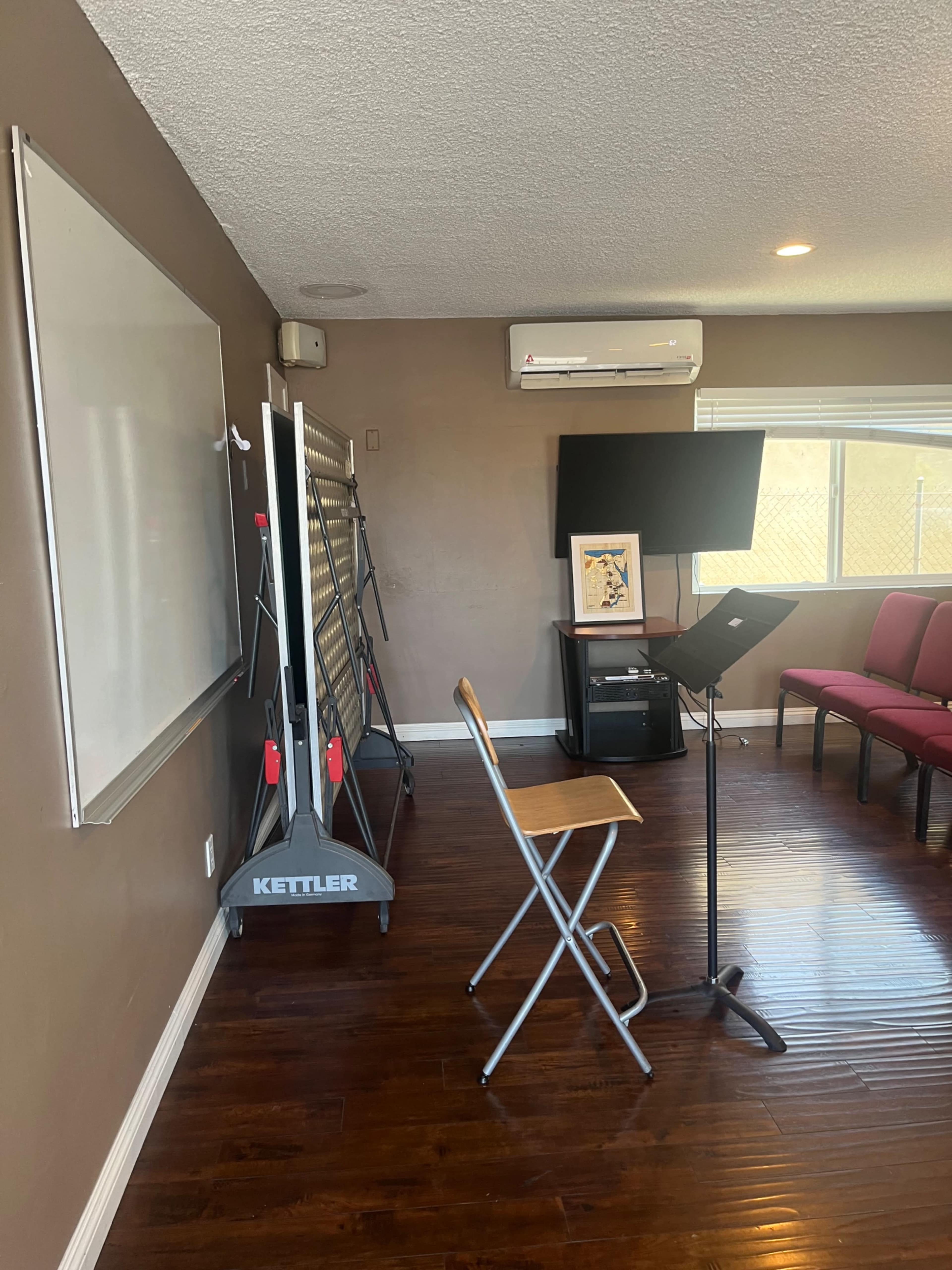 A meeting room featuring a whiteboard, a folding screen on wheels, a music stand, a wooden chair, and red upholstered chairs along the wall.