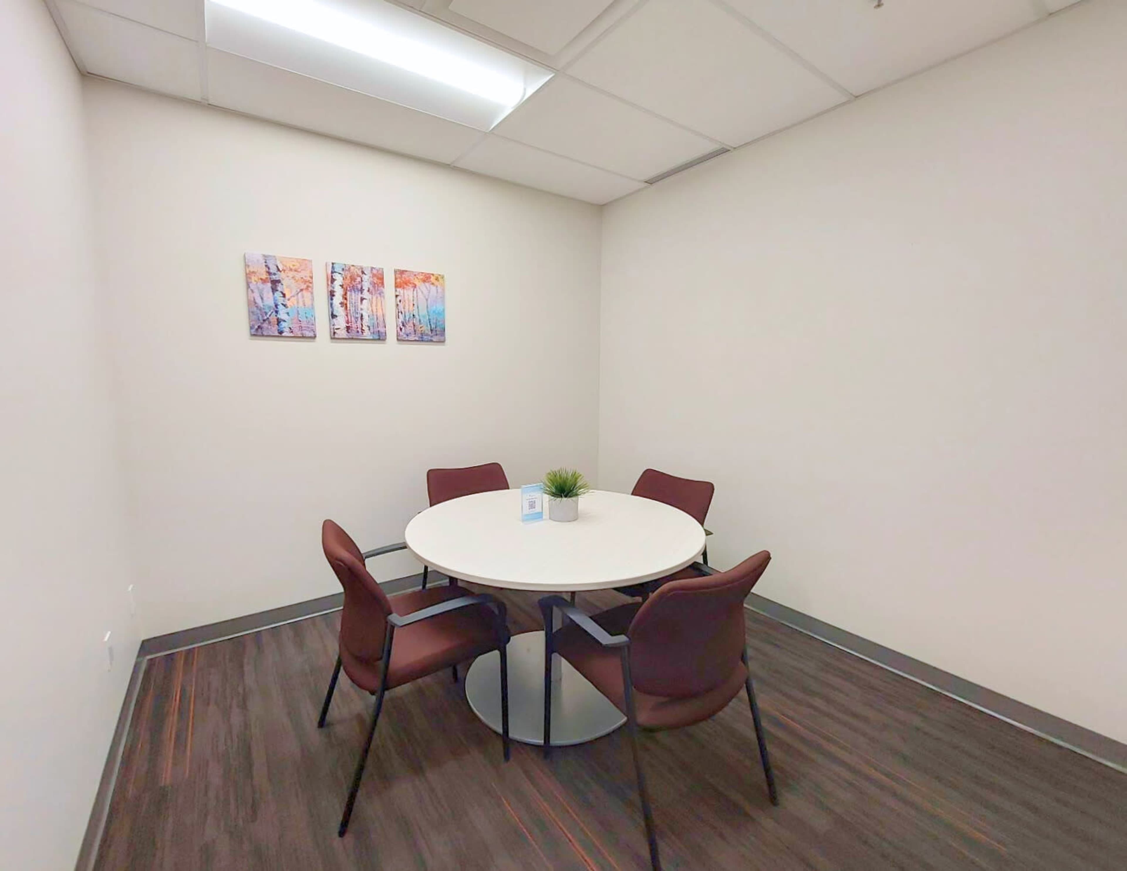 A small meeting room features a round table with four chairs and colorful artwork on the wall.