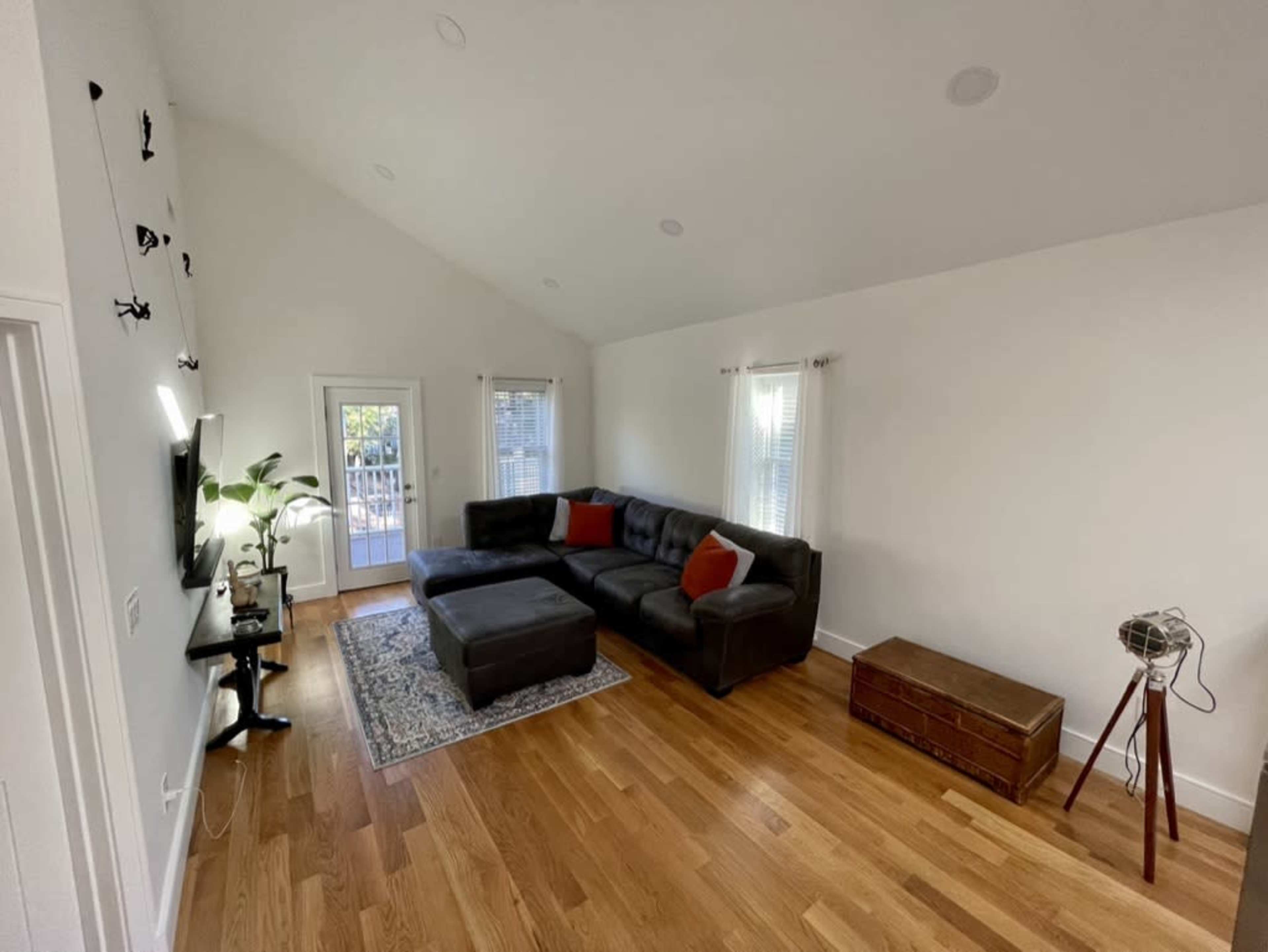 A modern living room features a dark sectional sofa, a wooden coffee table, and large windows allowing natural light.