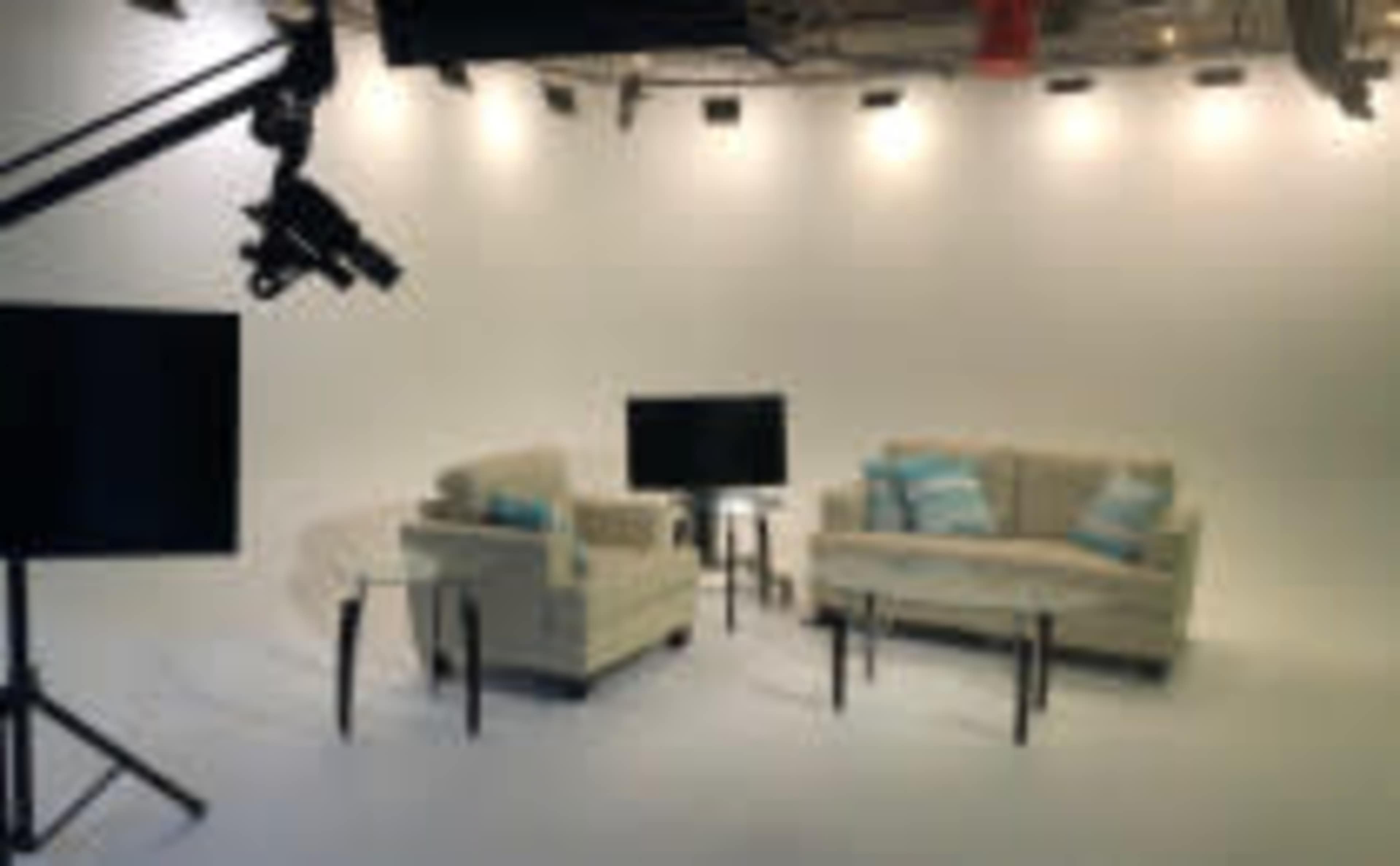 A two-sofa set with light cushions and a glass coffee table is arranged in a well-lit studio space.