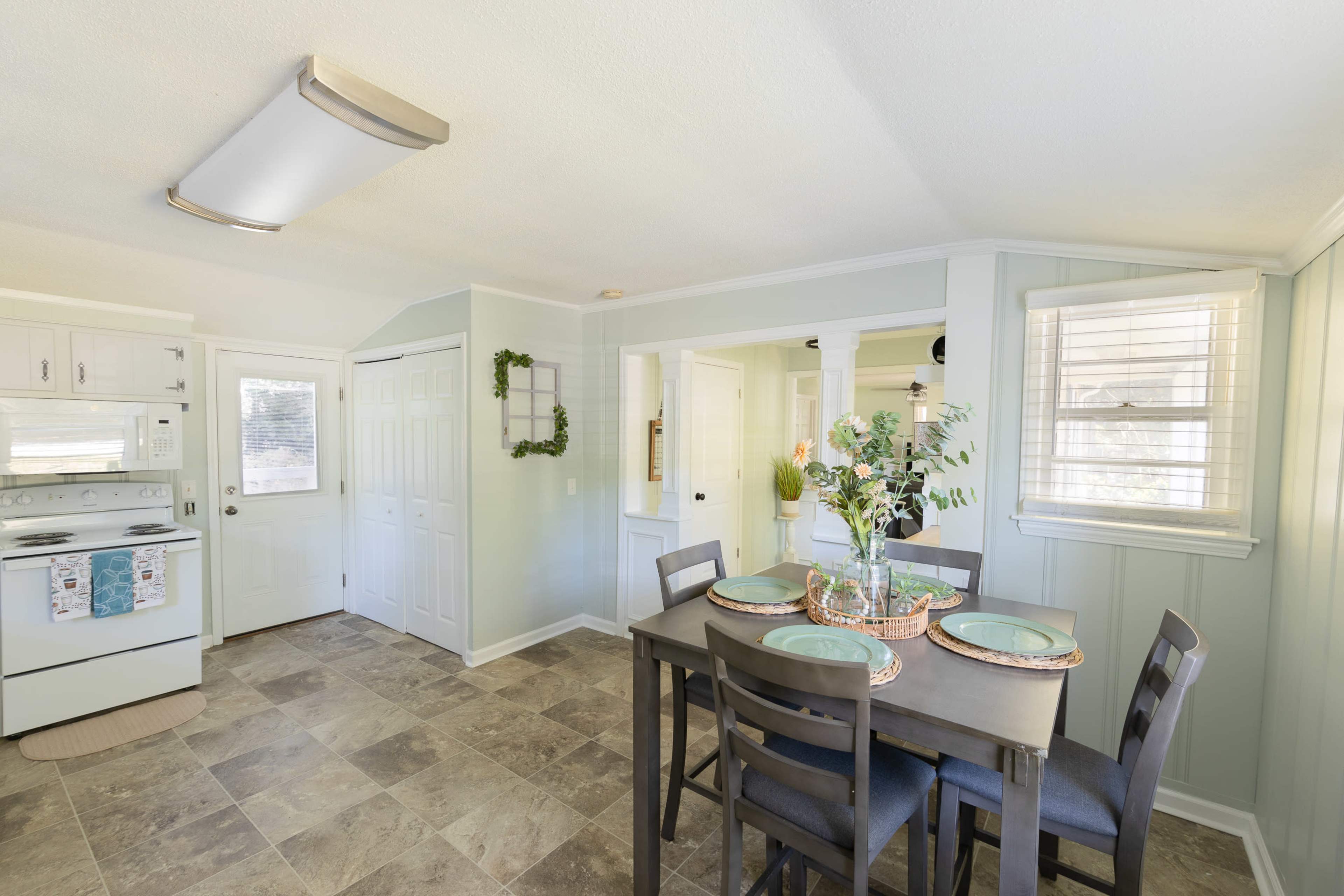 A small dining area with a table set for four is adjacent to a kitchen featuring white cabinetry and a door leading outside.