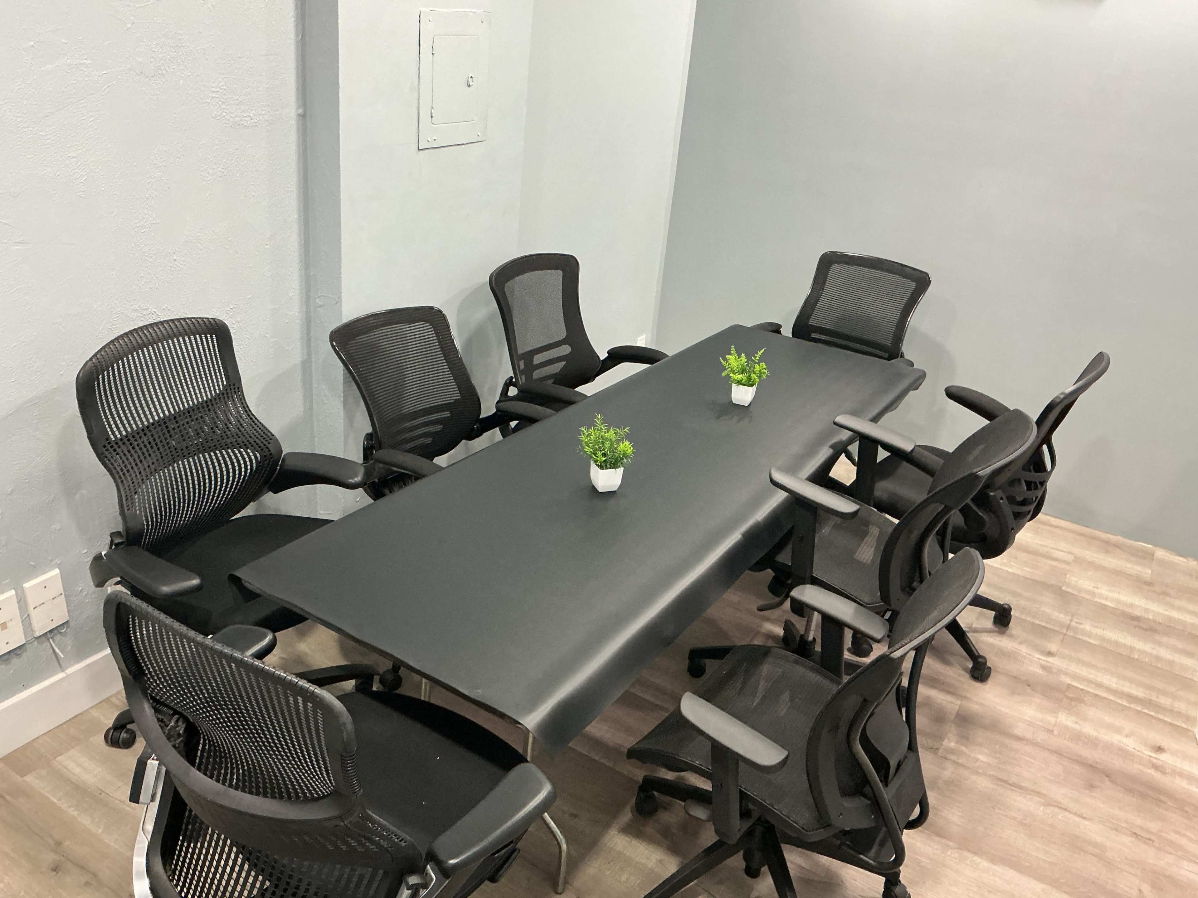A conference room with a long black table surrounded by several office chairs and small potted plants on the table.