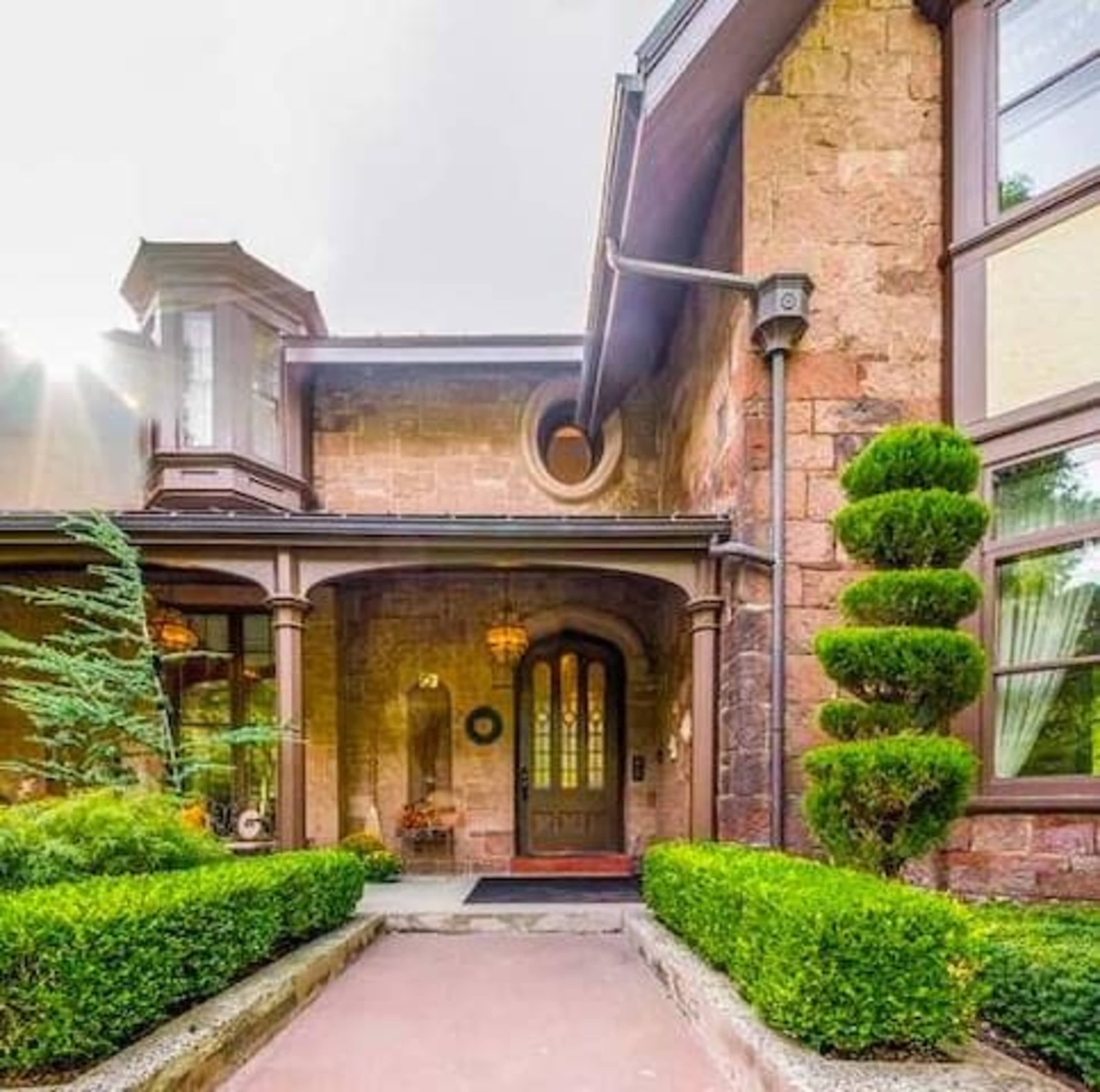 A stone house entrance with manicured shrubs, a pathway, and lanterns hanging from the porch.