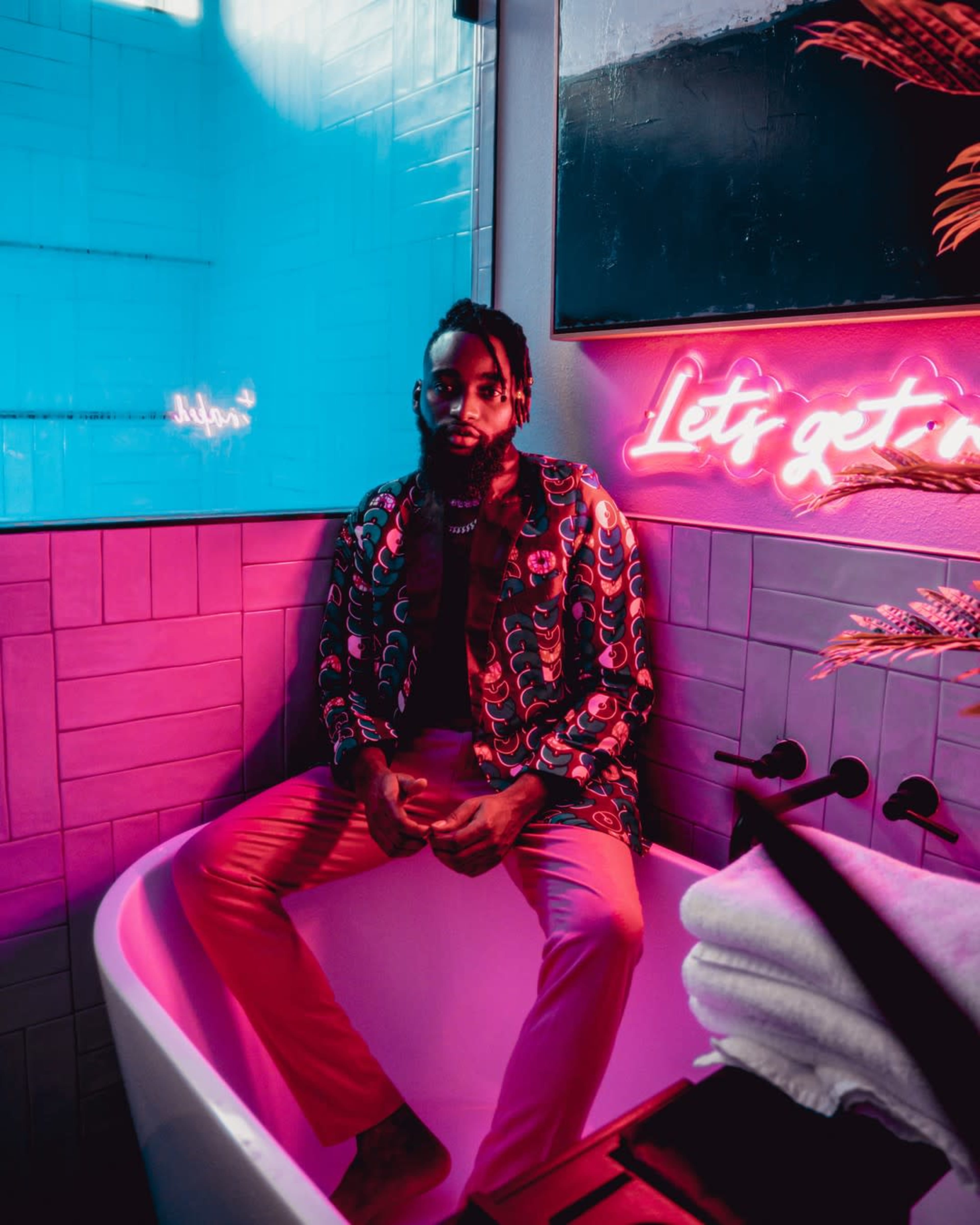 A man sits in a colorful bathtub surrounded by vibrant lighting and decorative elements.