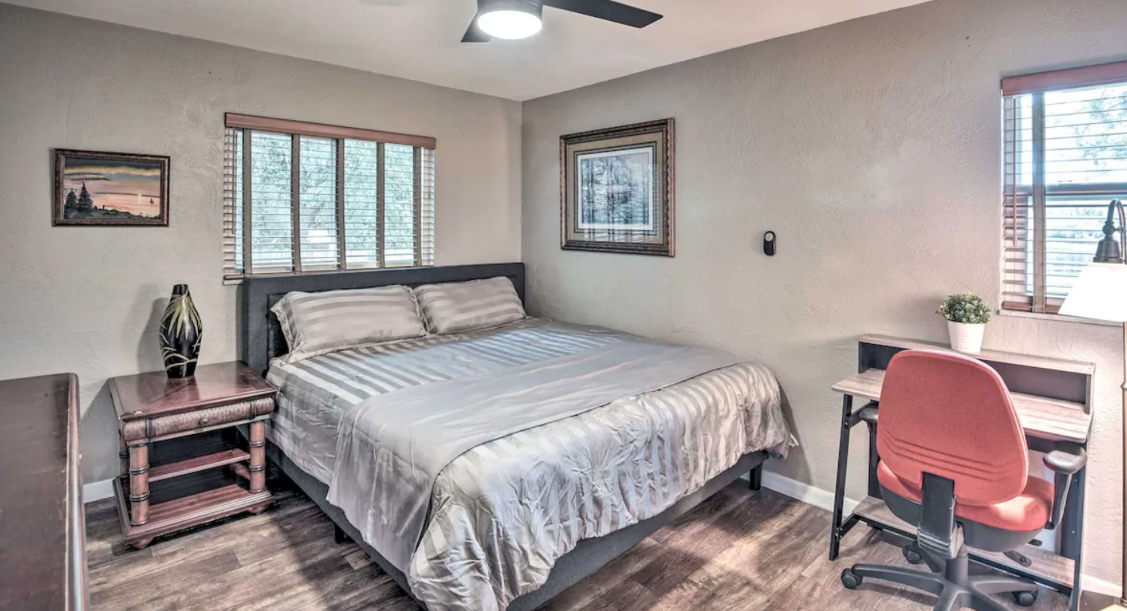 A bedroom with a large bed, a wooden nightstand, a desk with a chair, and framed artwork on the walls.