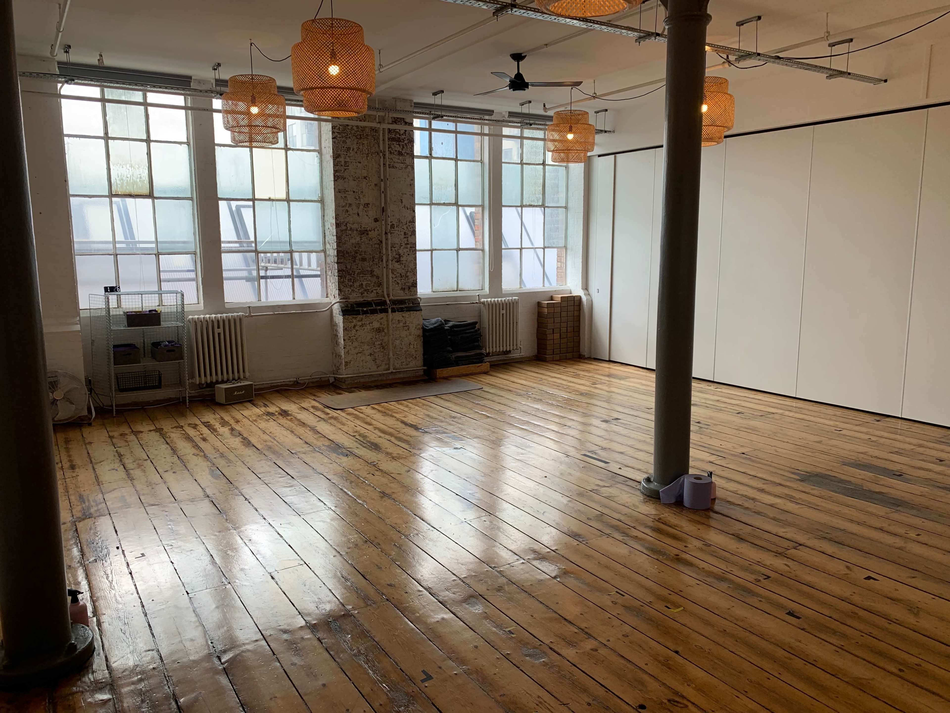 An empty room with wooden floors, large windows allowing natural light, and ceiling lamps made of woven material.
