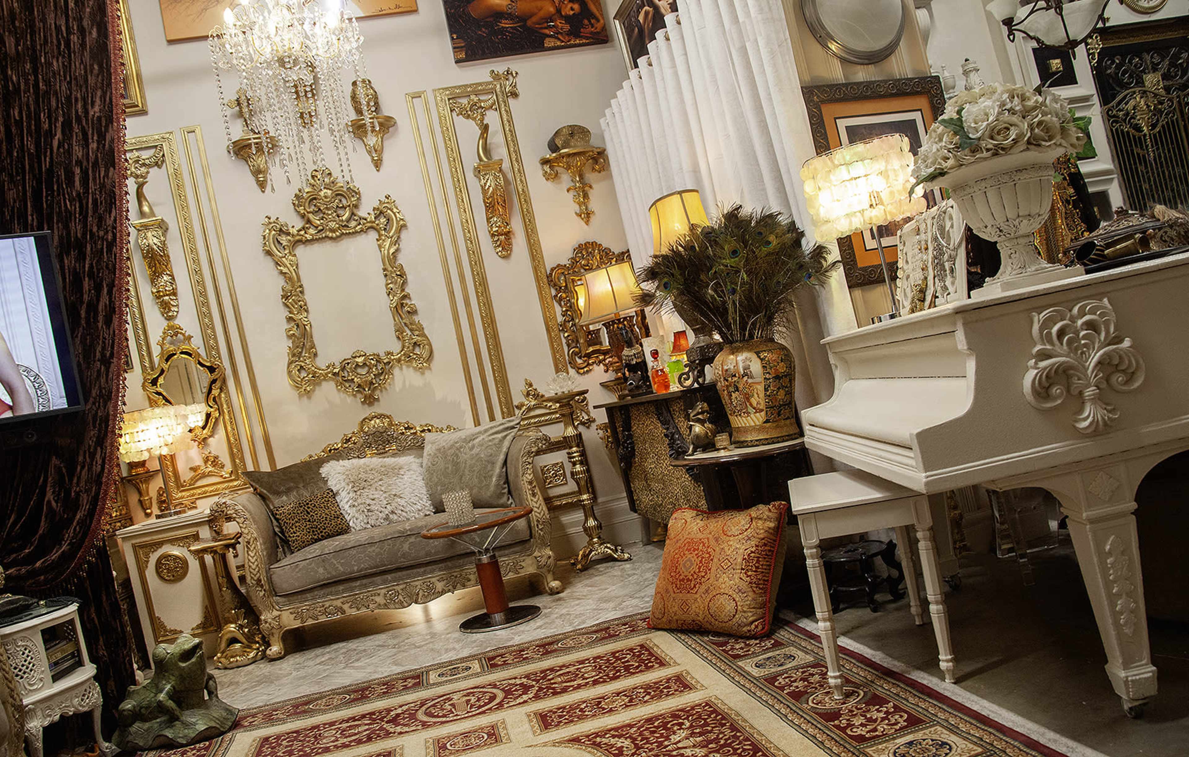 The image depicts a lavishly decorated room featuring ornate golden frames, a white piano, a plush sofa, and various decorative items arranged against a richly textured backdrop.
