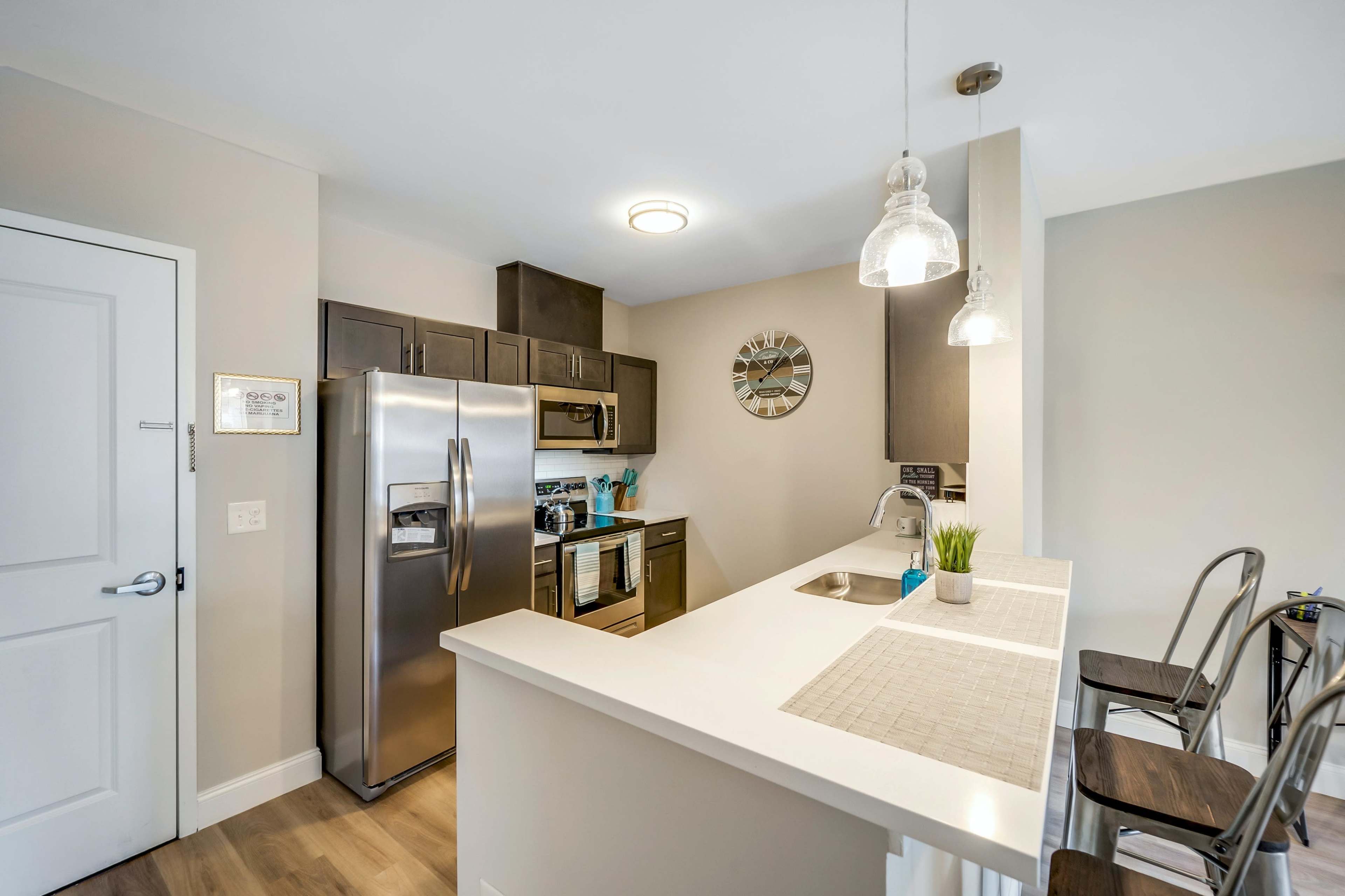 A modern kitchen with stainless steel appliances, a light-colored countertop, and bar seating.
