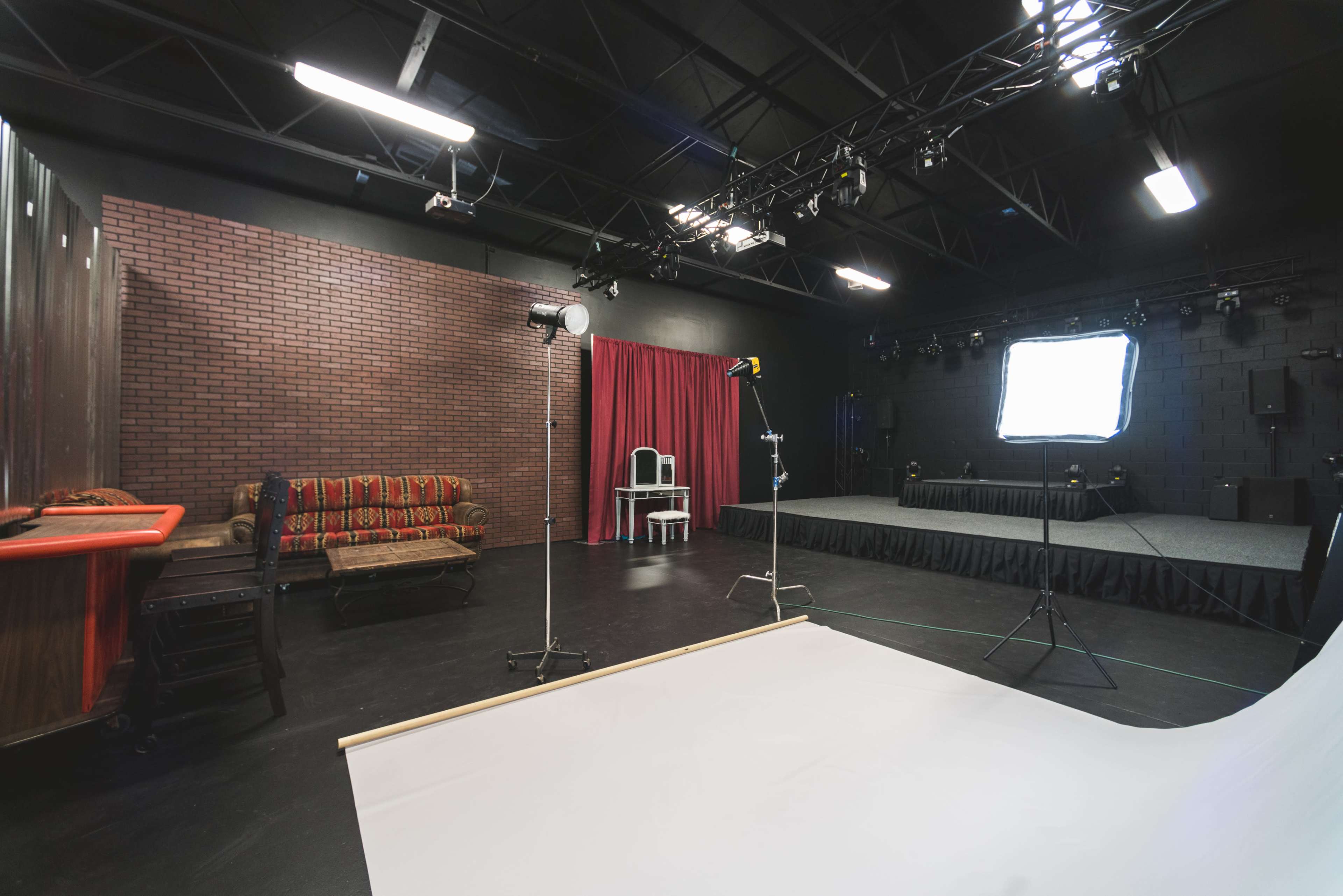 A photography studio featuring a brick wall backdrop, a couch, a white backdrop on the floor, and various lighting equipment.