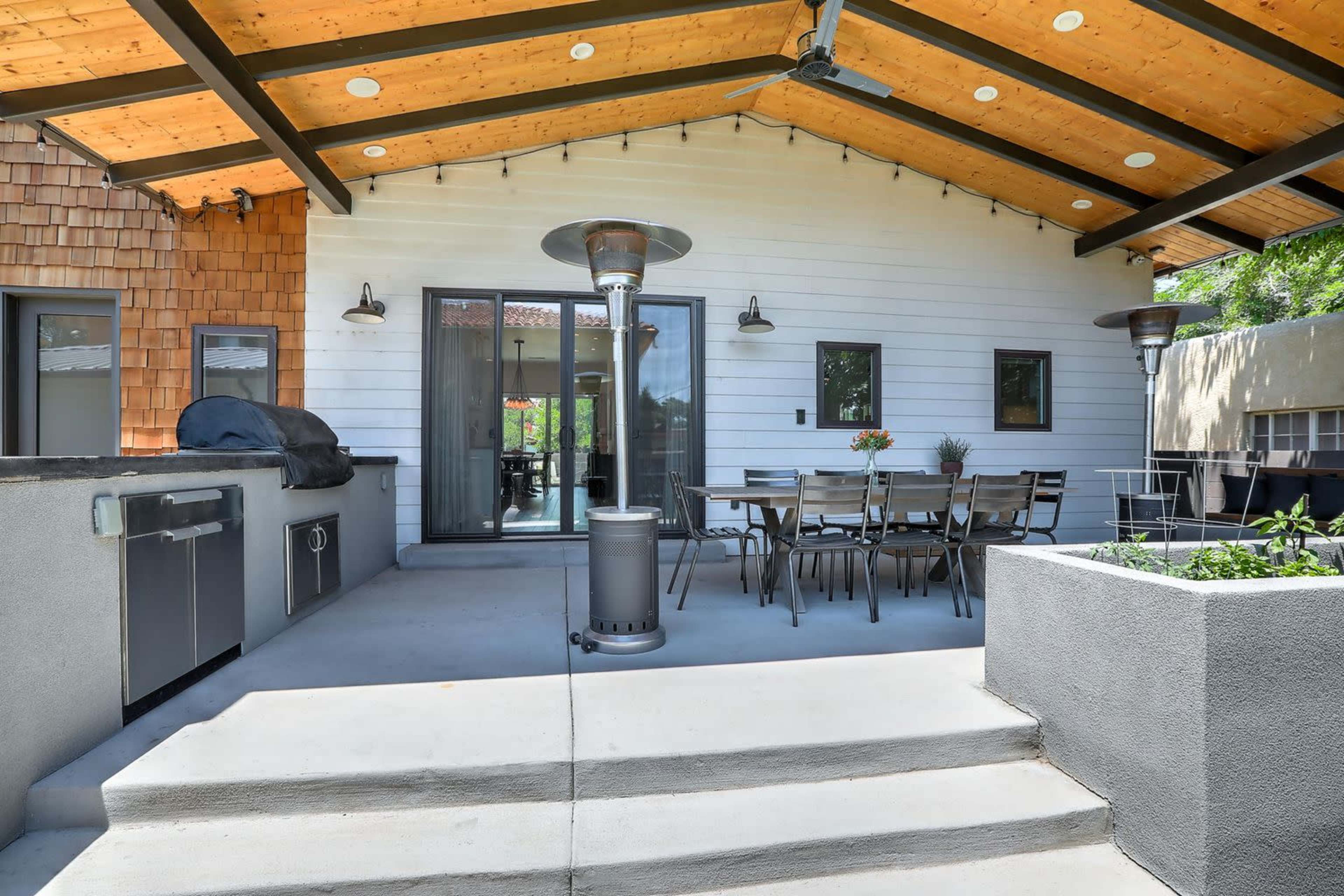 The image shows an outdoor patio area with a dining table, two heating lamps, a built-in grill, and a stepped entrance.