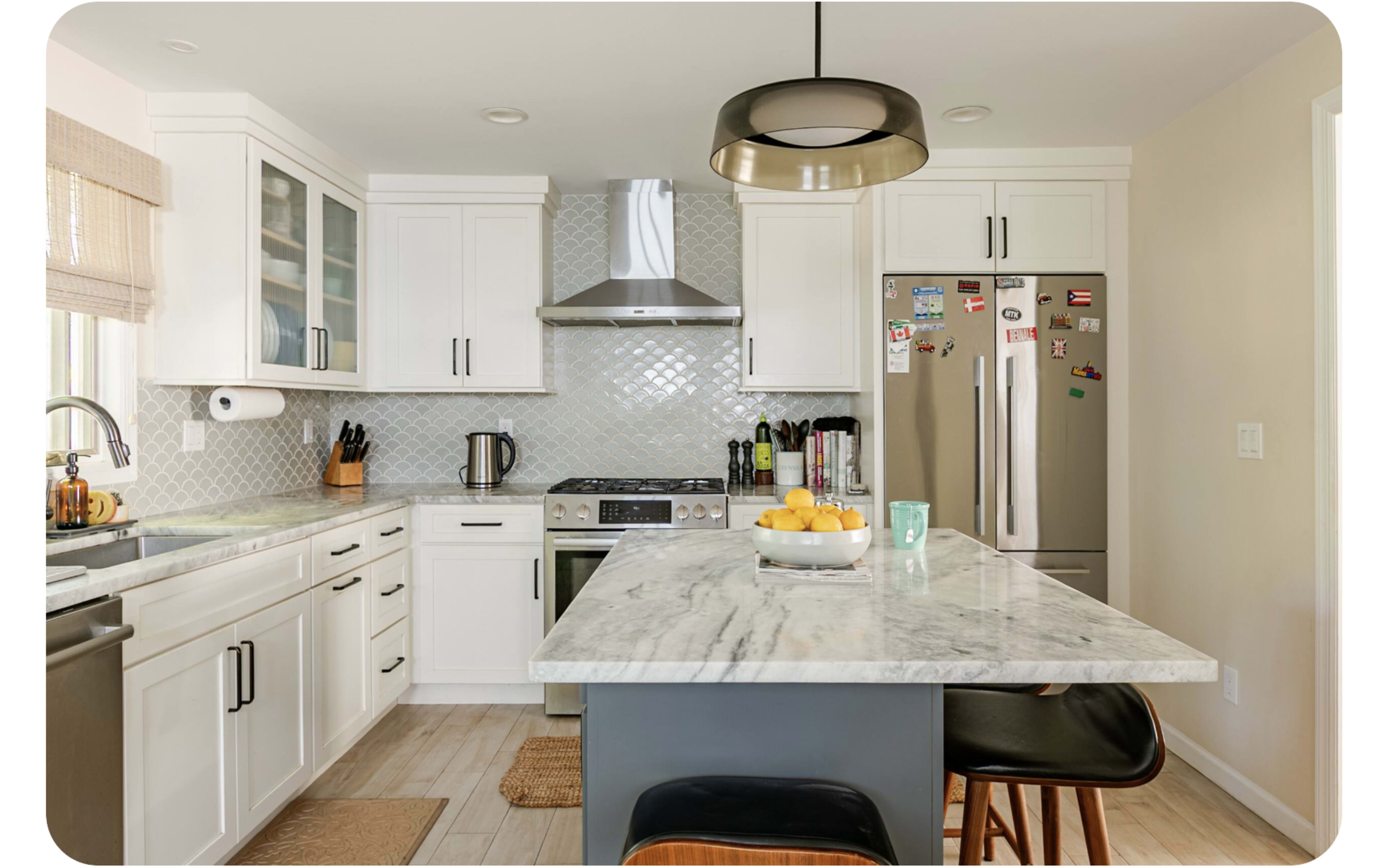 The kitchen features white cabinetry, stainless steel appliances, a marble island with a bowl of oranges, and modern pendant lighting.
