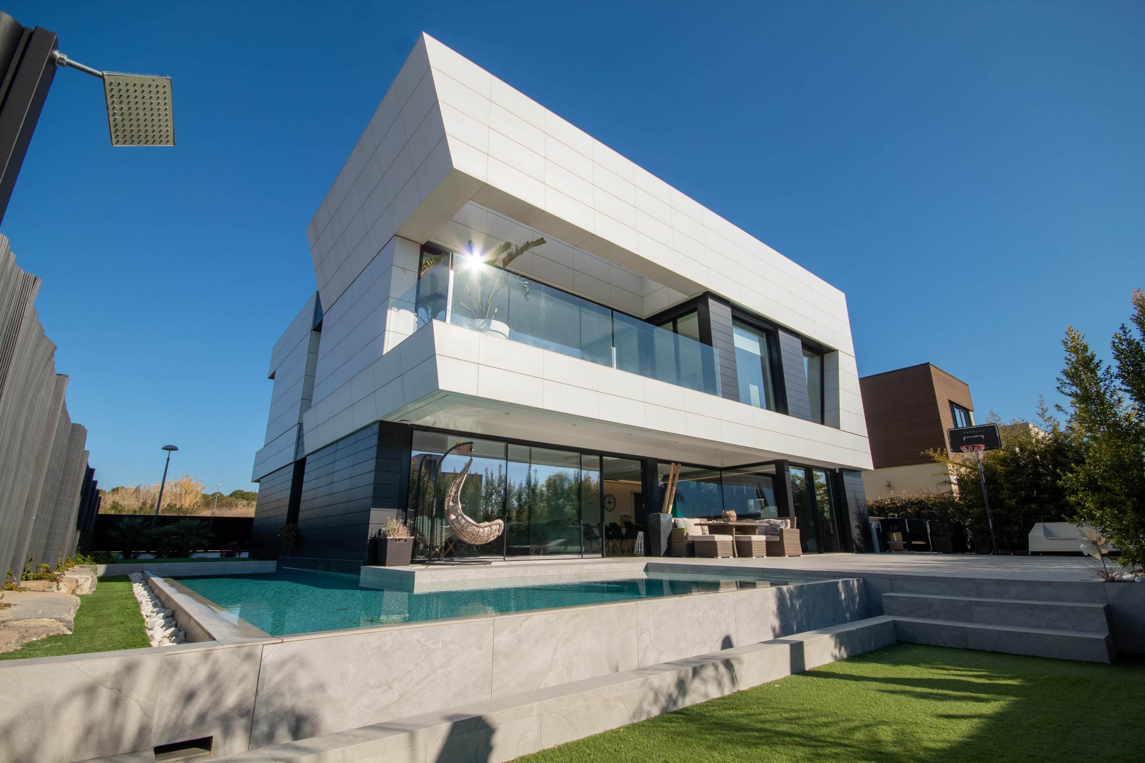 A modern house with a sleek white exterior, large glass windows, and a pool in the backyard.