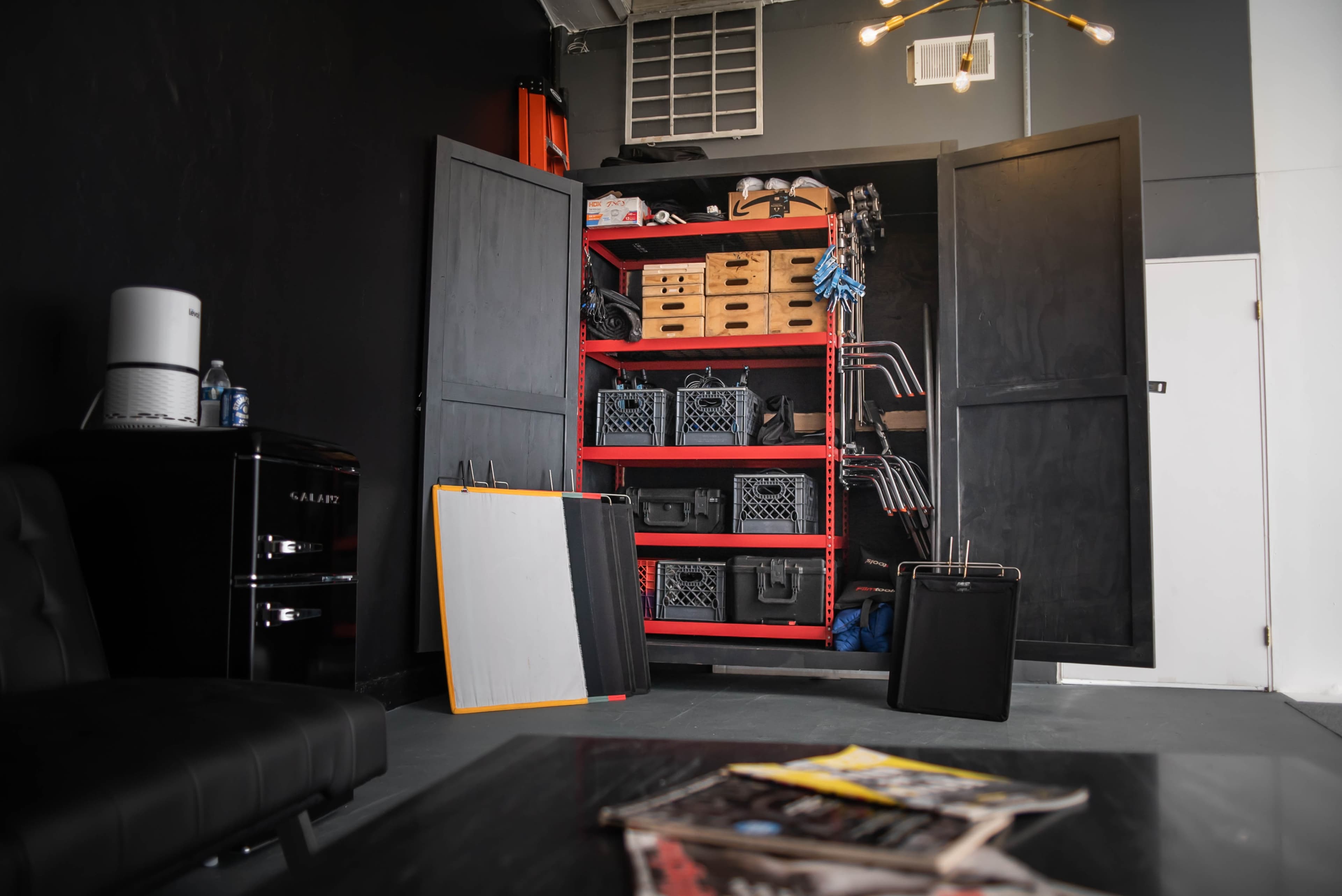 A storage area features a red shelving unit filled with boxes and equipment, alongside a black couch and a small fridge.