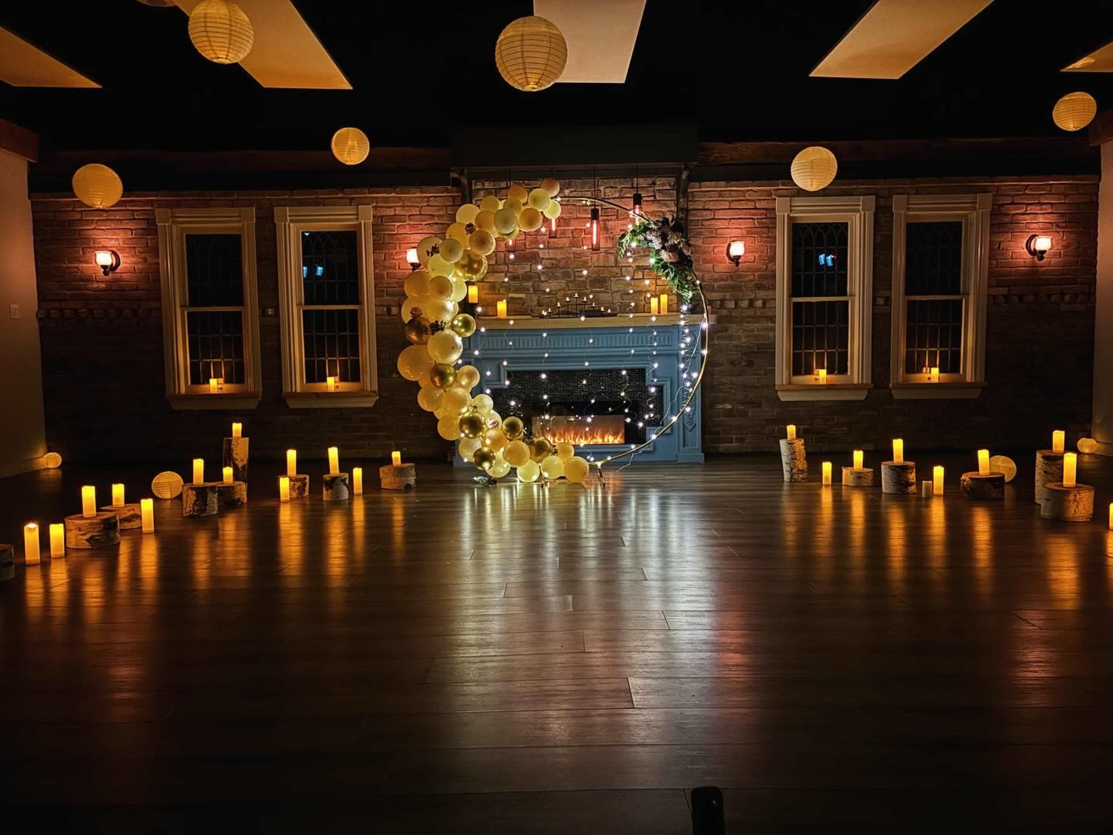 A decorated indoor space with a blue fireplace surrounded by candles, lanterns, and a crescent-shaped balloon arrangement.